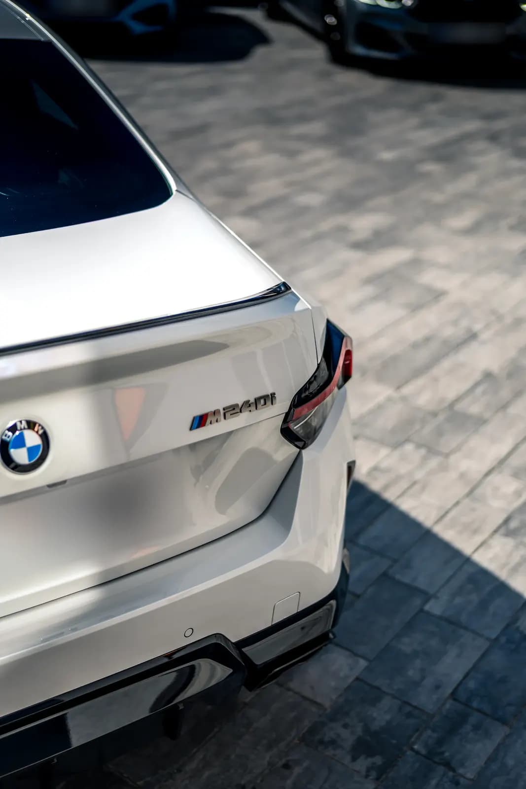 Detail zadní části bílého BMW M240i s logem M240i a spoilerem na víku kufru.