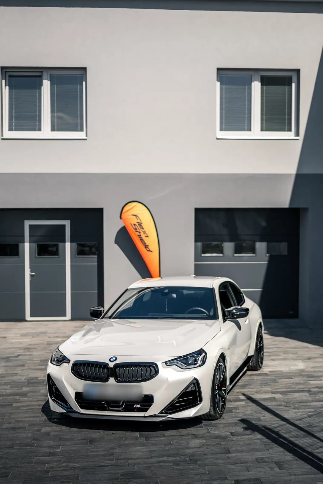 Bílé BMW M240i zaparkované před provozovnou Seven Works, boční přední pohled.