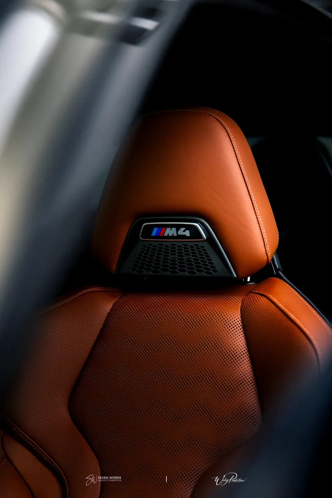 Detail opěrky hlavy sedadla BMW M4 s logem M4 v hnědé kůži.