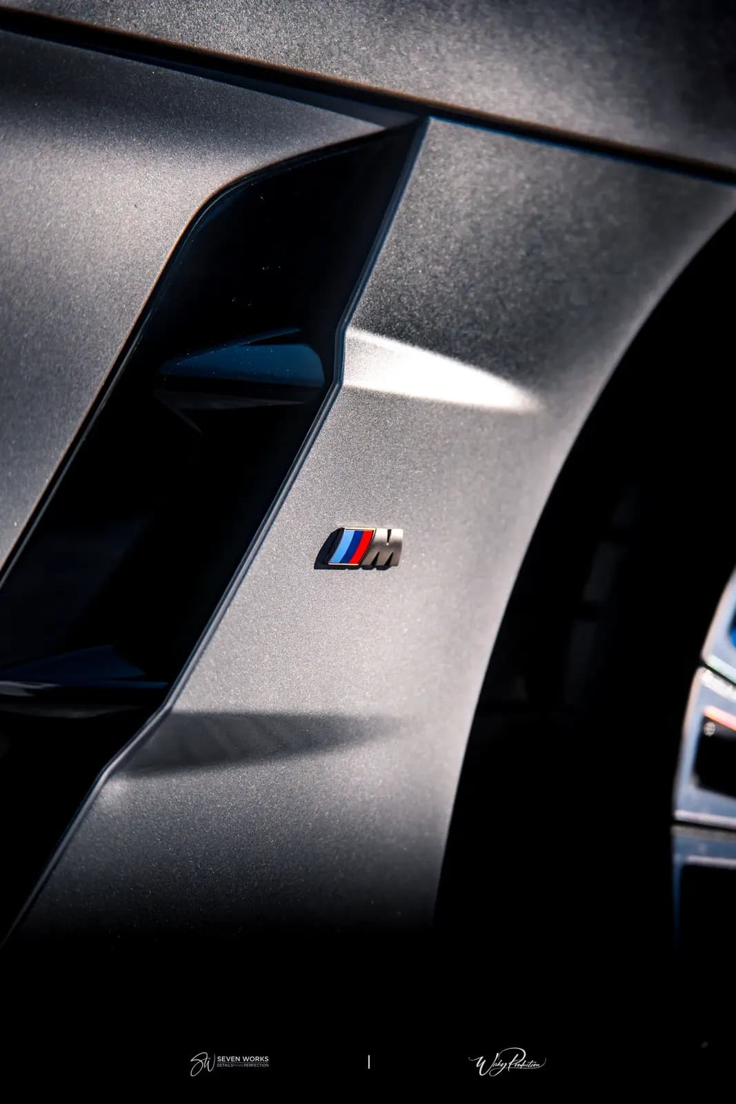 Makro detail loga BMW M na boku karoserie v dramatickém nasvícení.