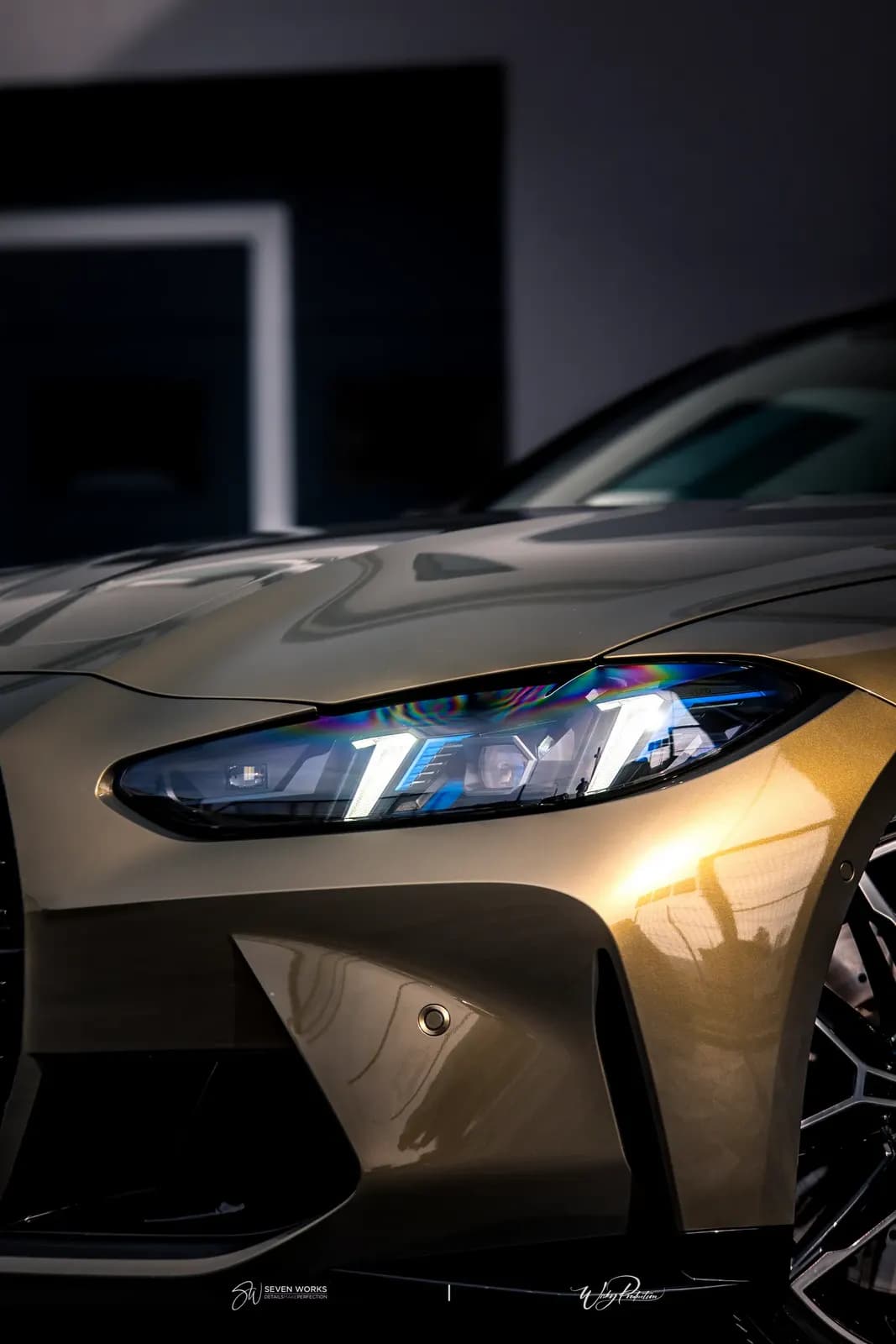 Makro detail předního světla zlatavého BMW M4 s barevnými odlesky.