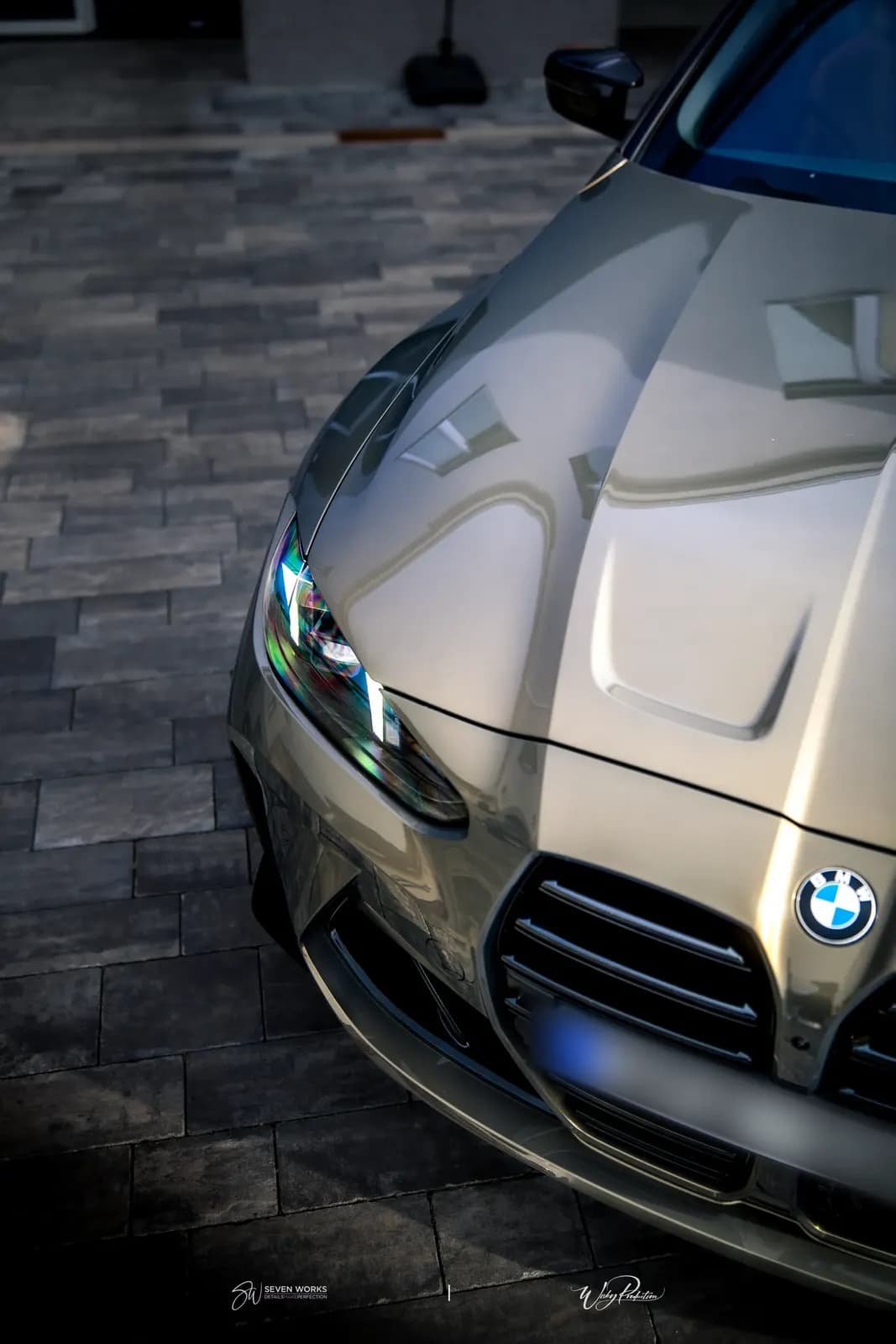 Detail kapoty, světla a masky zlatavého BMW M4 s dlažbou v pozadí.
