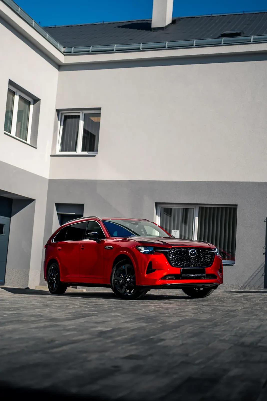 Červená Mazda CX SUV zaparkovaná před budovou provozovny pod modrou oblohou.