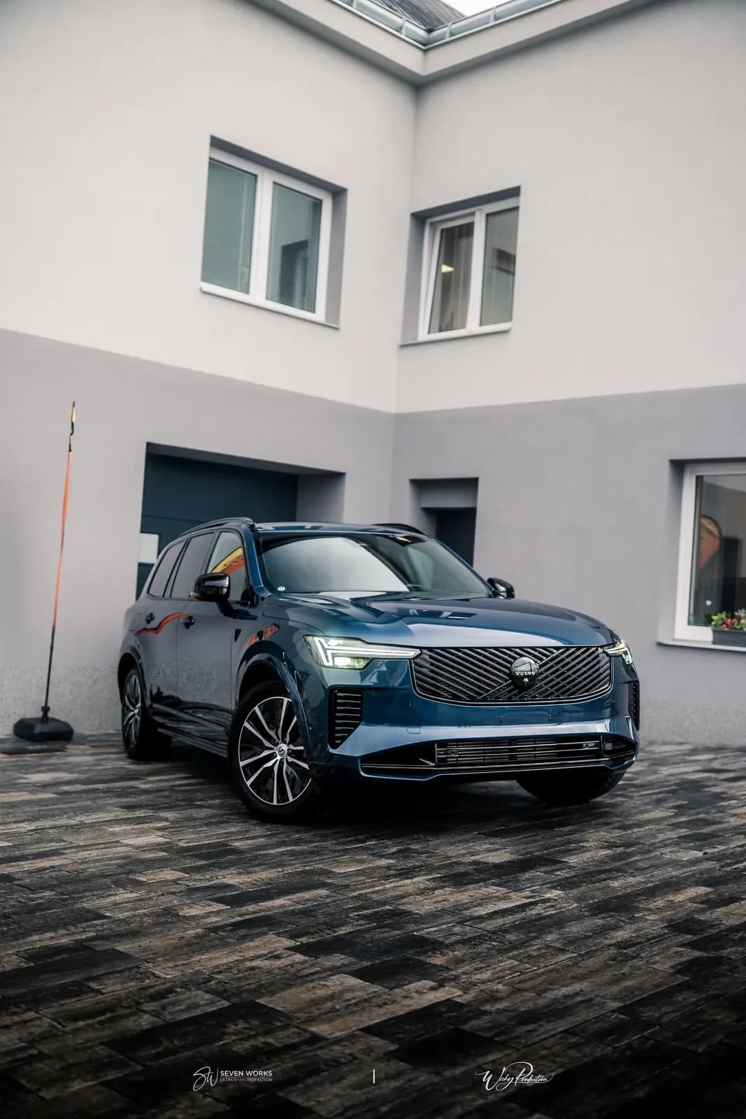 Modré Volvo XC90 zaparkované před provozovnou za soumraku.