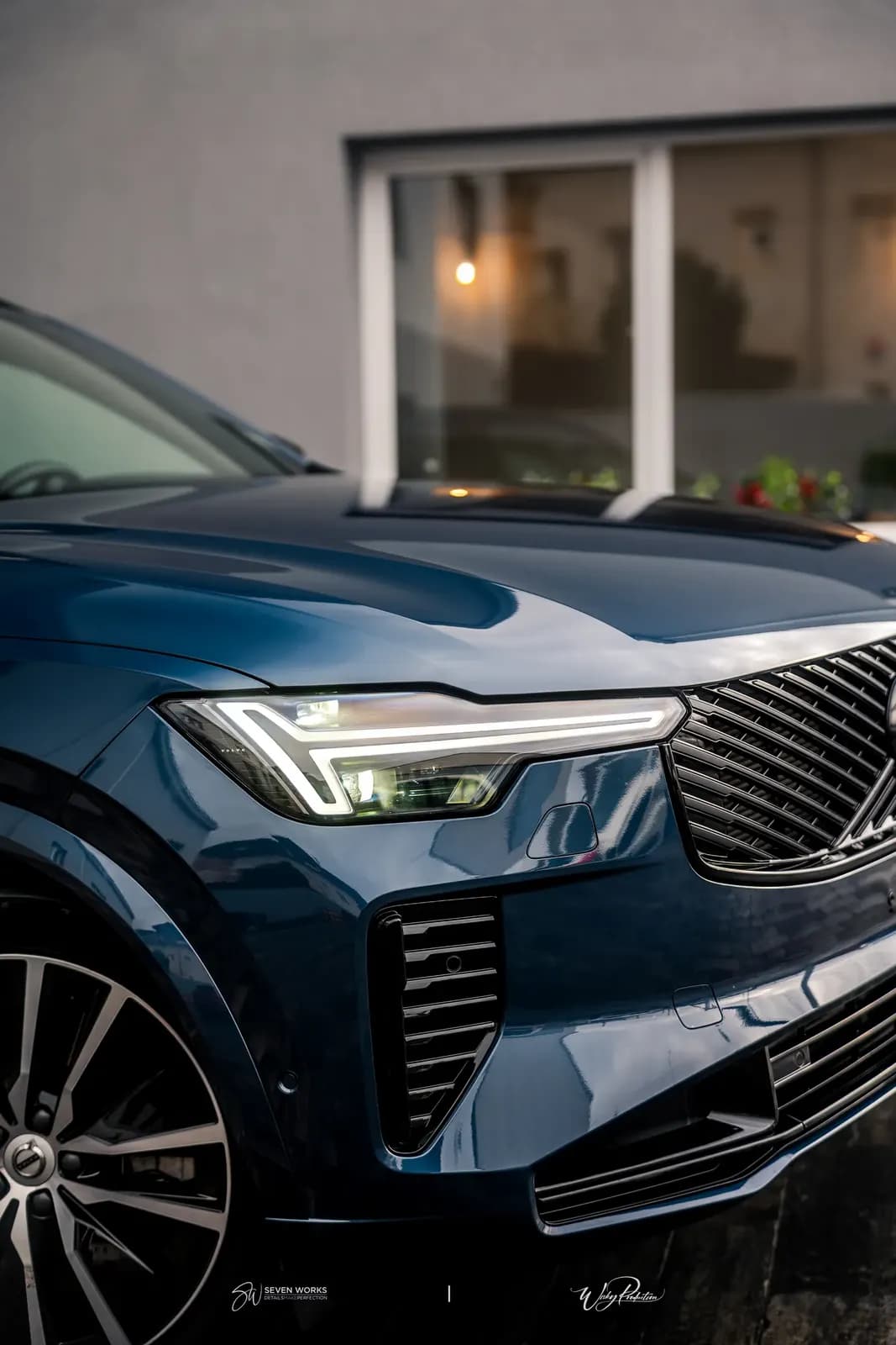 Detail kapoty a předního světla modrého Volvo XC90 za soumraku.
