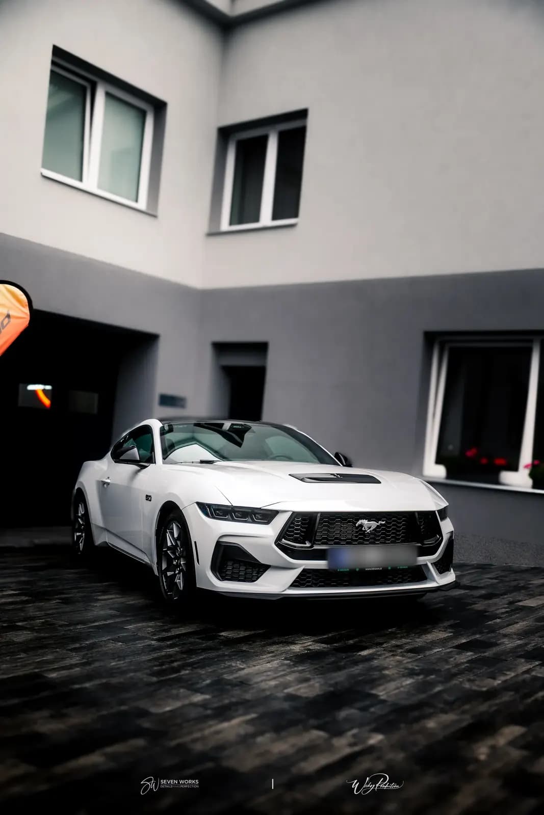 Bílý Ford Mustang ze tří čtvrtin zepředu před budovou dílny.