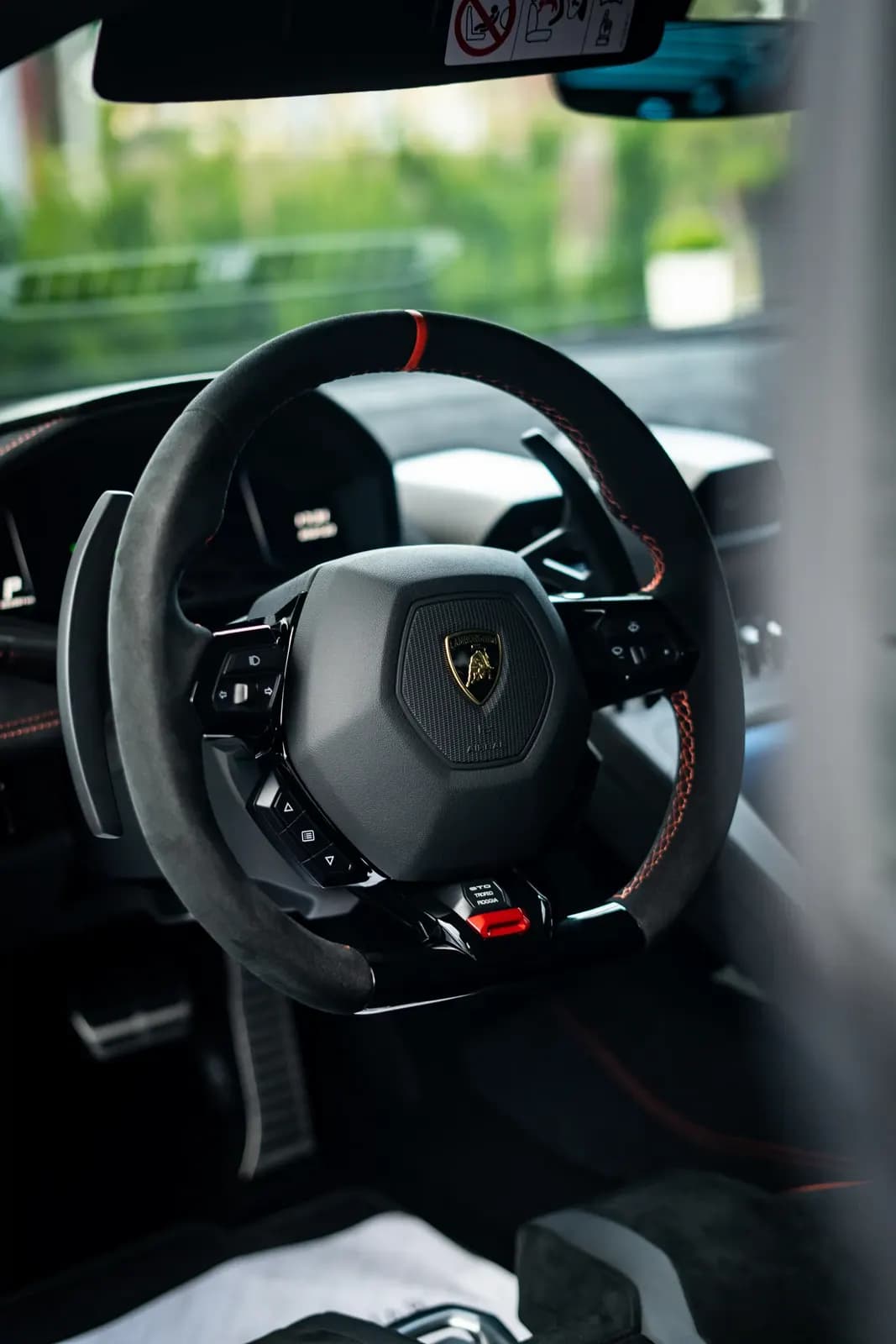 Volant Lamborghini s logem výrobce a červeným detailem, pohled z interiéru.