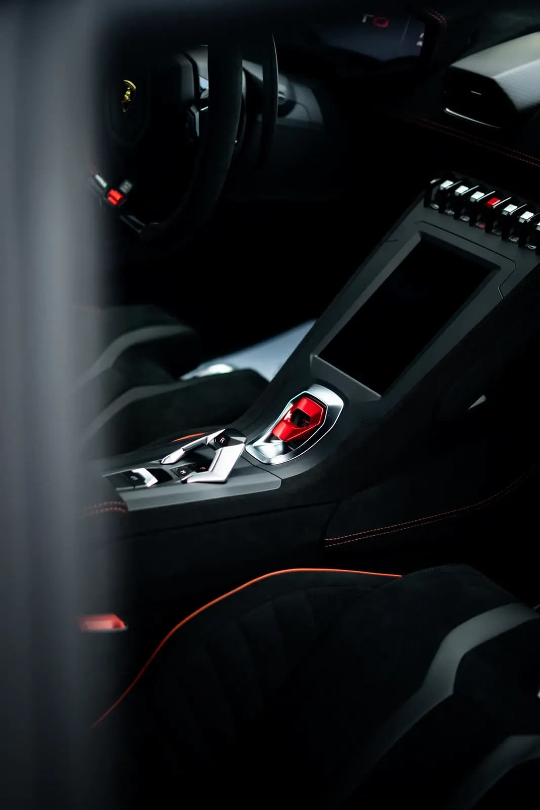 Interiér Lamborghini s volantem a středovým panelem, pohled přes rozostřené popředí.