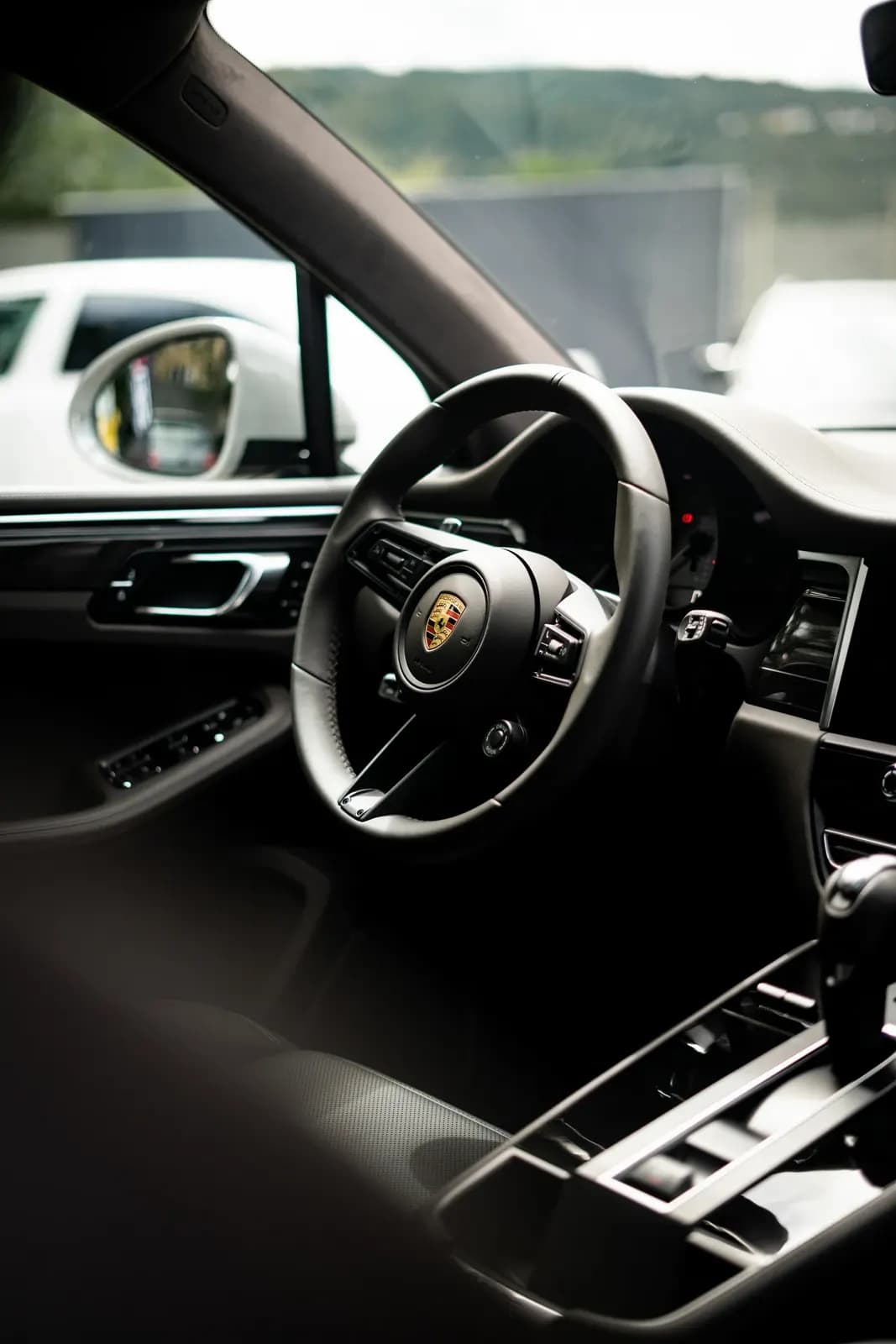 Pohled do interiéru Porsche otevřenými dveřmi, volant s logem Porsche.