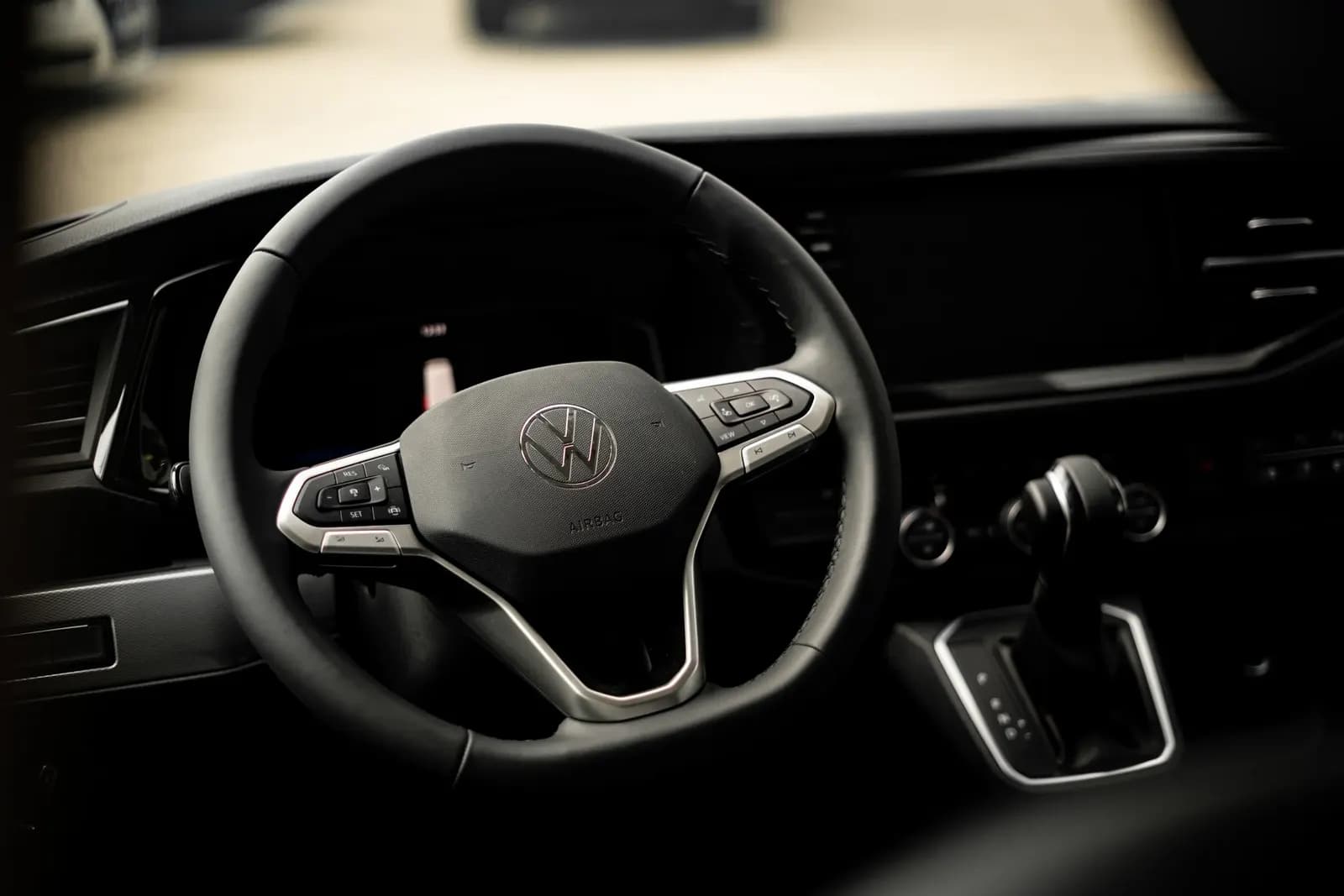 Volant Volkswagen v interiéru vozu, v pozadí rozostřená ulice.