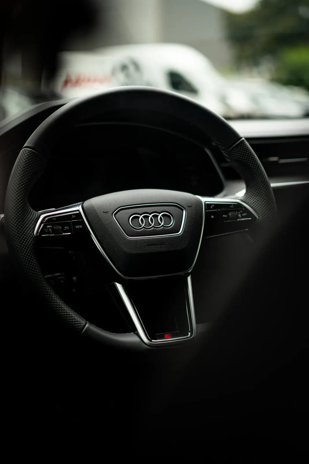 Volant Audi s logem výrobce, v pozadí rozostřená dodávka.
