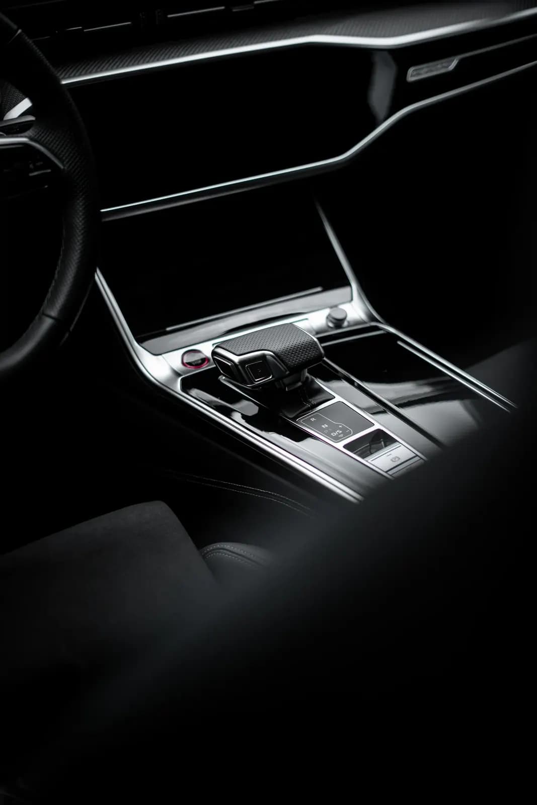 Tmavý středový panel Audi s displejem a řadicí pákou.