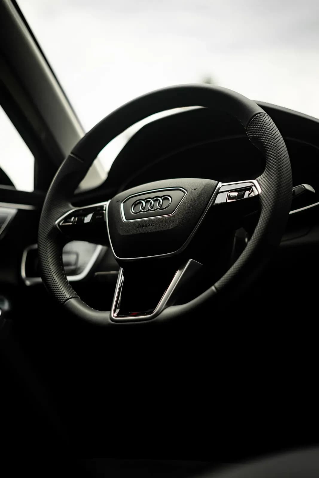 Volant Audi s logem výrobce, v pozadí zatažená obloha.