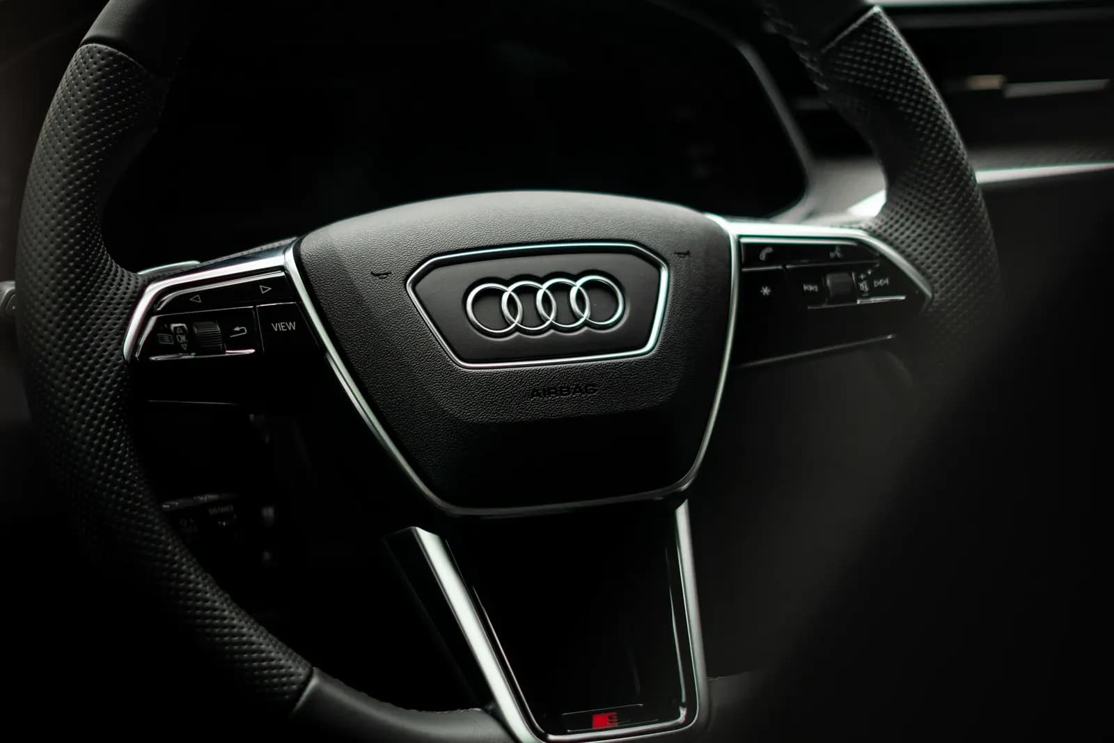 Detail volantu Audi se středovým logem čtyř kruhů, pohled zevnitř vozu.