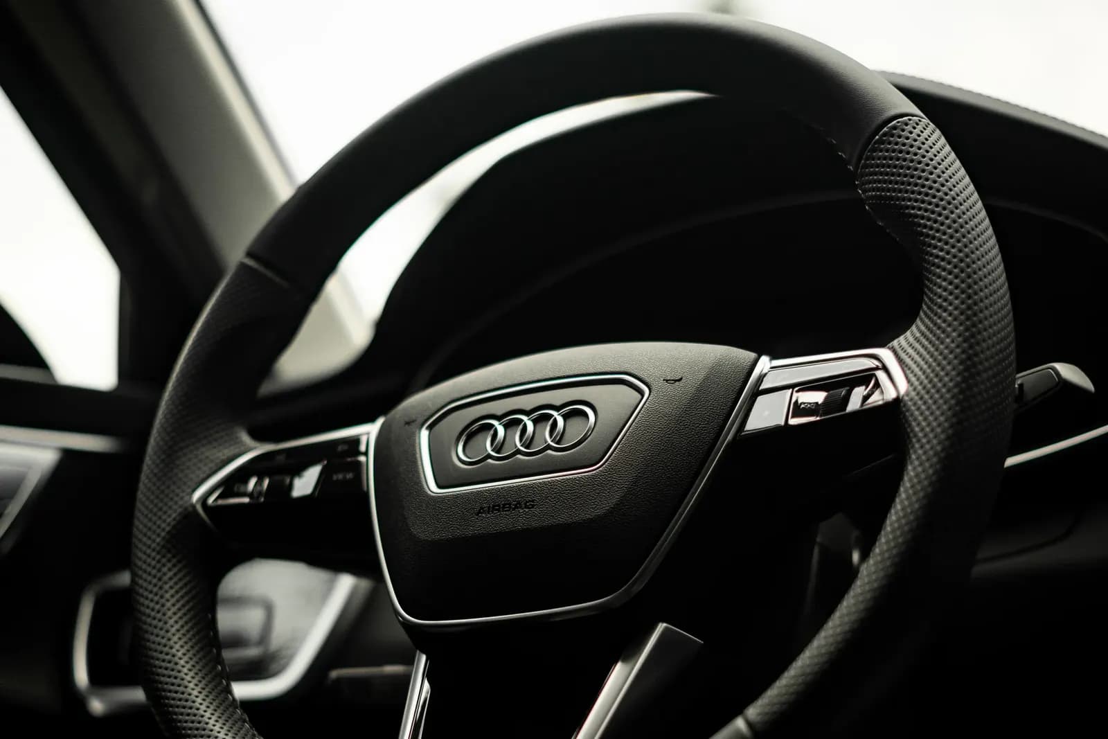 Audi steering wheel with the four-ring logo, shot from the driver’s door against the light.