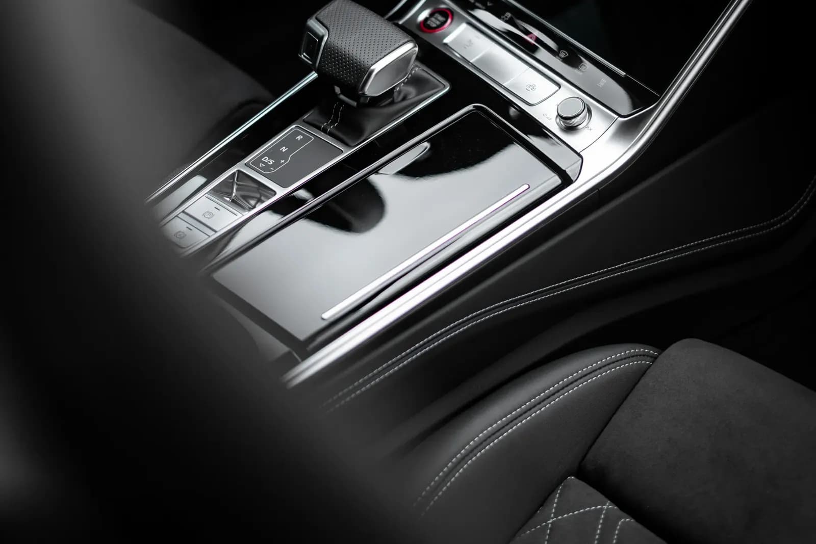 Close-up of a glossy centre console and gear selector next to a stitched seat.
