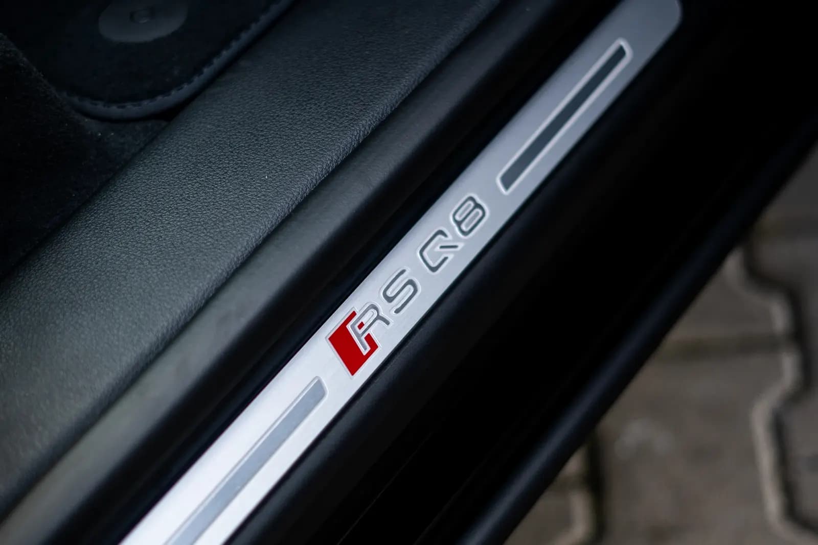 Close-up of a door-sill plate with the RS Q8 badge by the open car door.