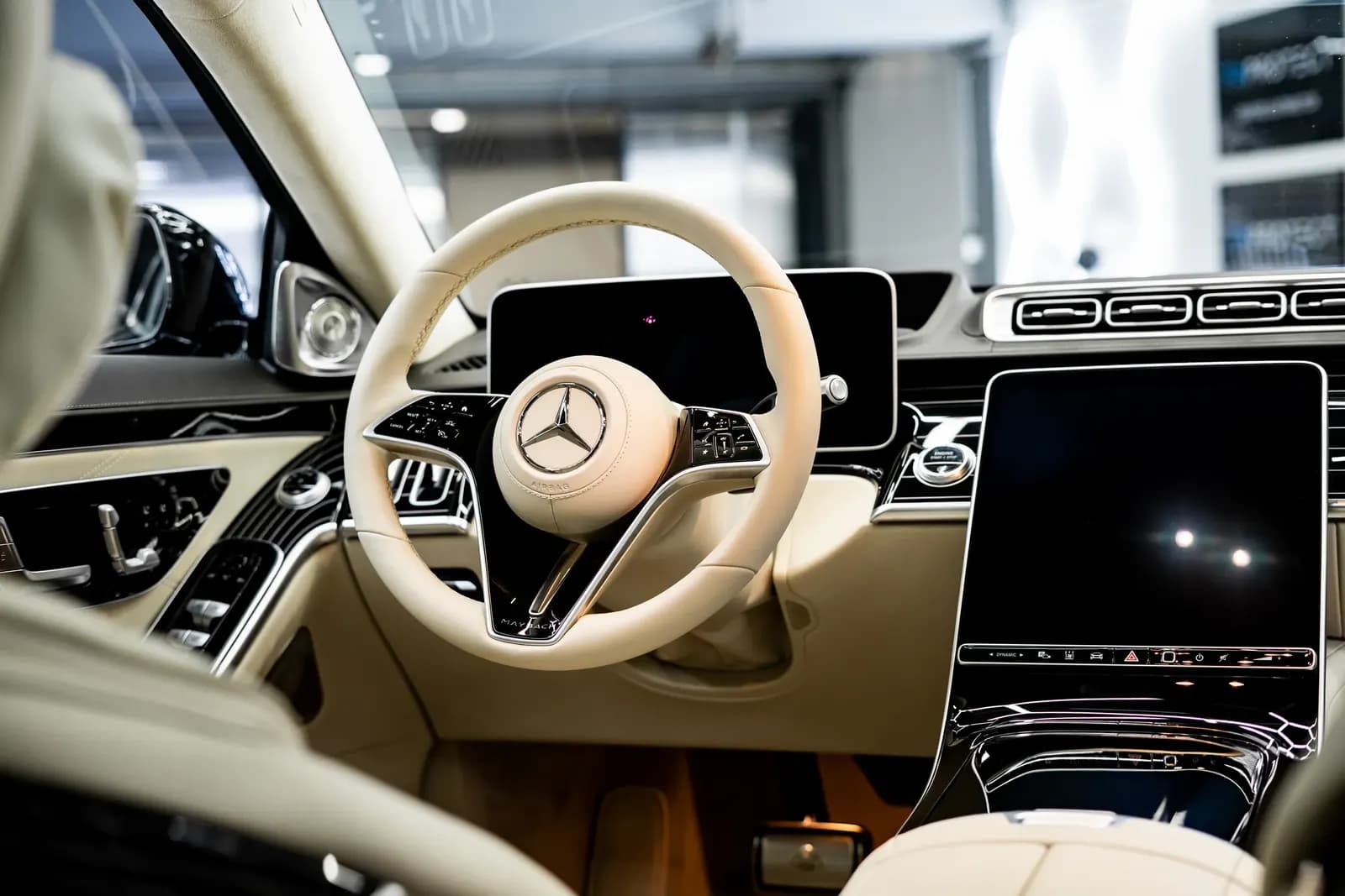Interior of a Mercedes-Maybach with a light-coloured steering wheel and two dashboard screens.