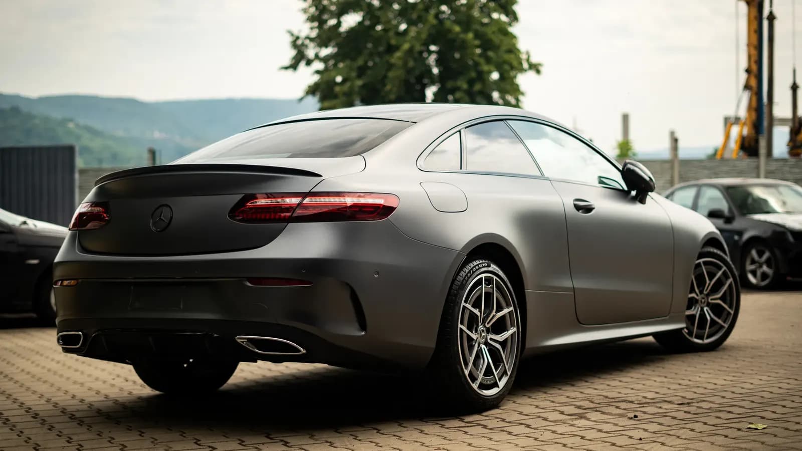 Rear three-quarter view of a matte grey Mercedes-AMG coupe outdoors with hills in the background.