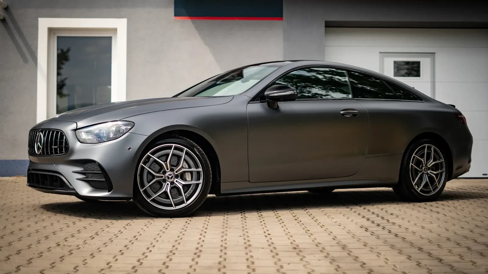 Matte grey Mercedes-AMG coupe parked in front of a building, side view.