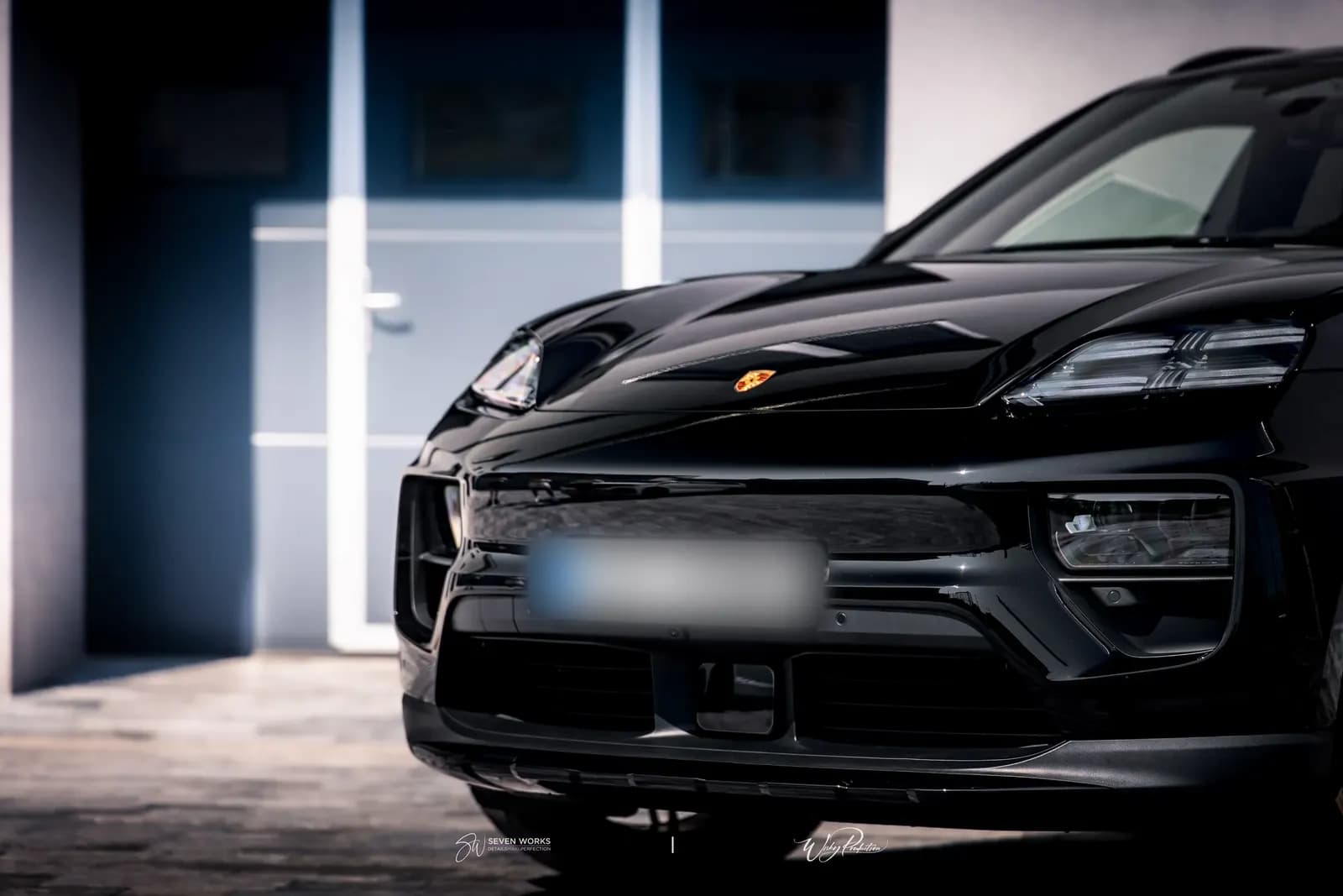 Close-up of the front fascia and headlights of a black Porsche against a grey facade.