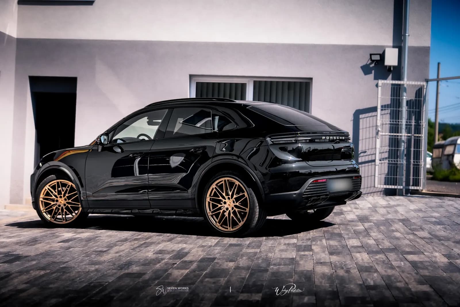 Rear section of a black Porsche with the Porsche wordmark and bronze wheels, side view.