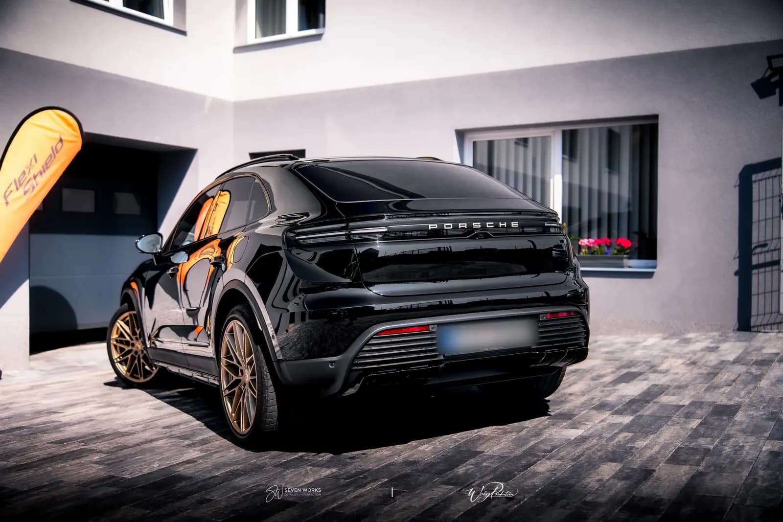 Rear three-quarter view of a black Porsche with the lettering on the tailgate and bronze wheels.