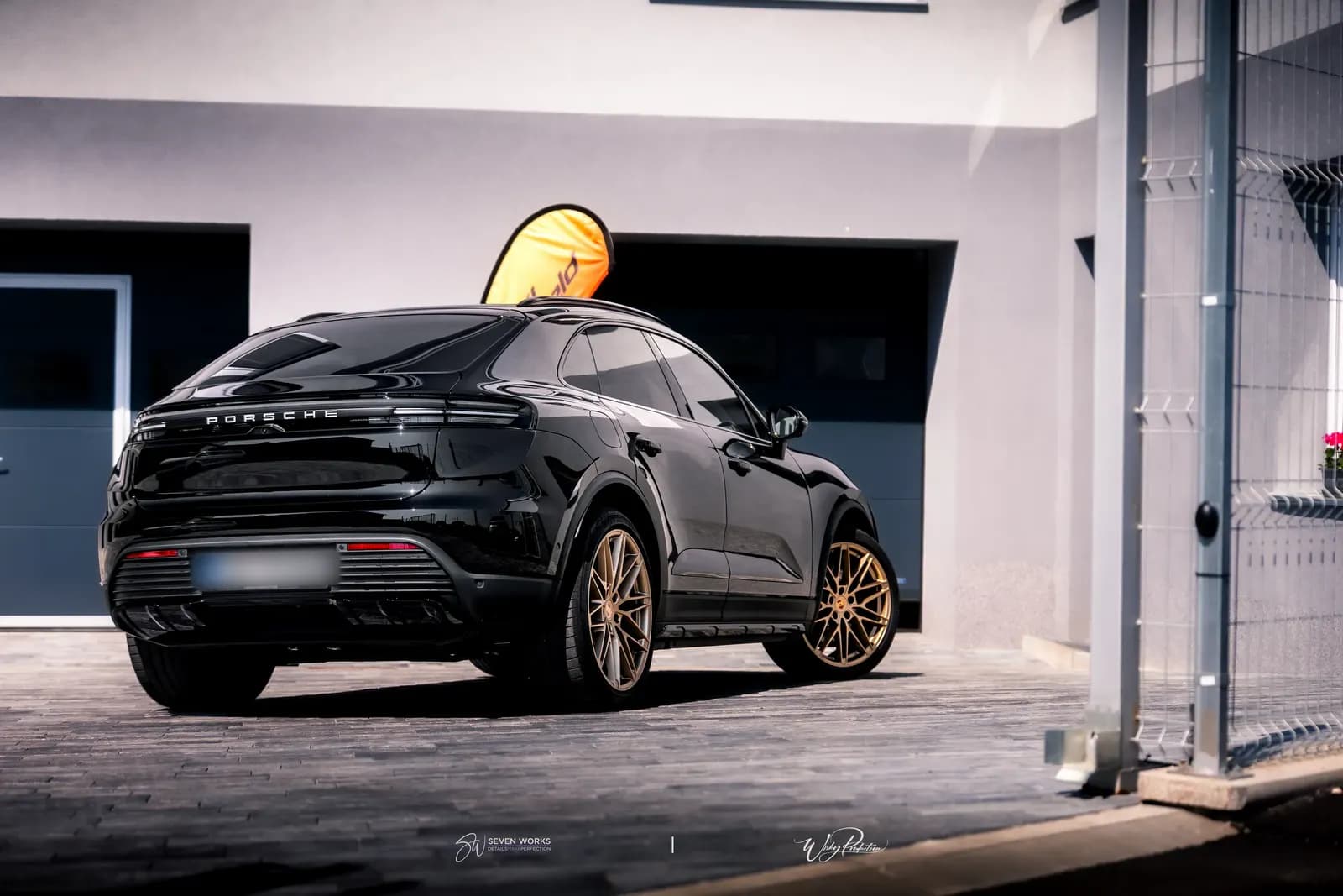 Rear view of a black Porsche with a FlexiShield flag and a mesh fence in the background.