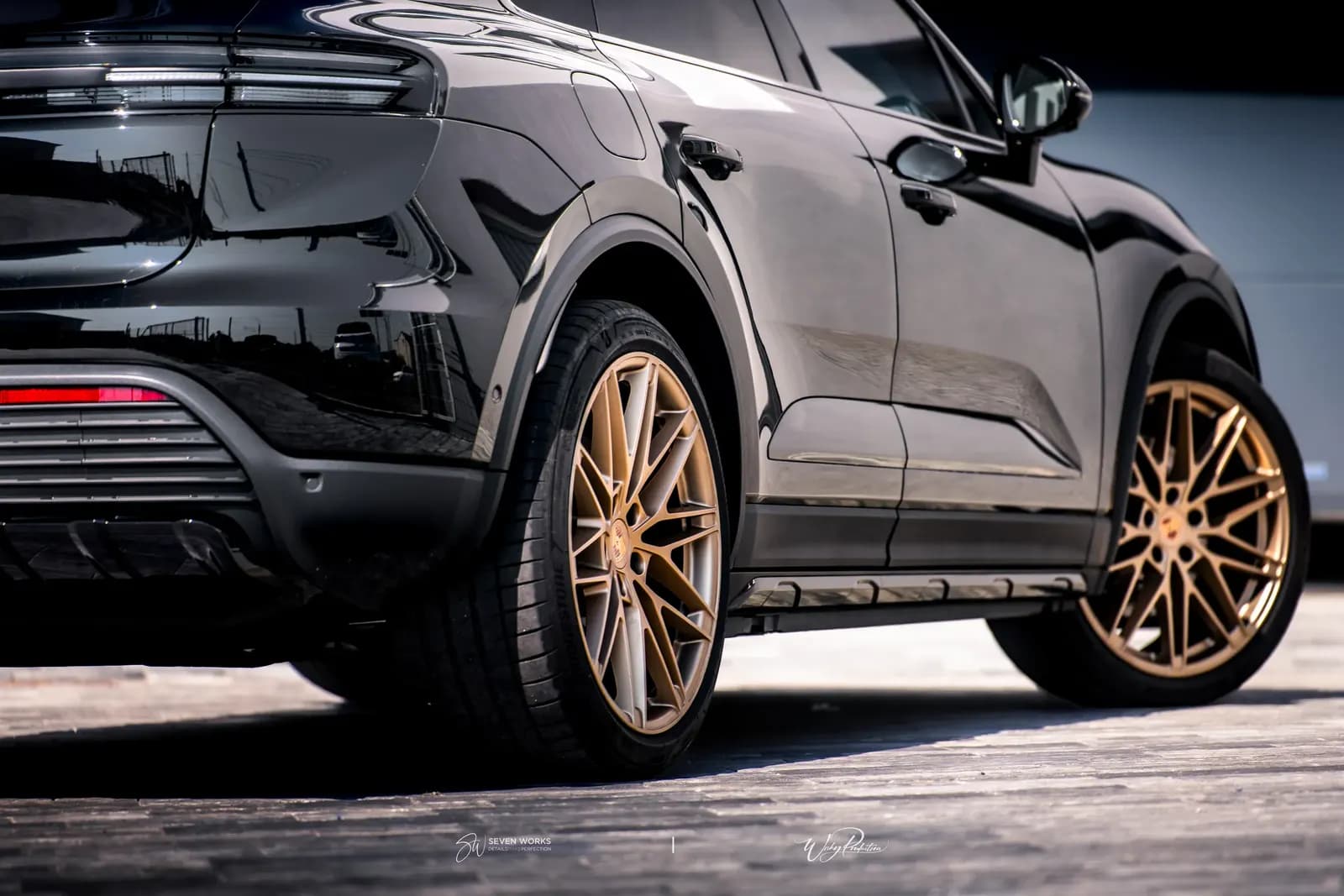 Close-up of the rear wheel of a black Porsche with gold alloy wheels.