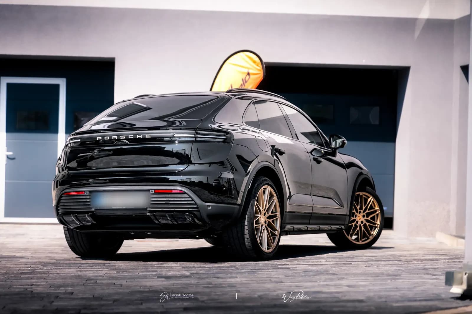 Black Porsche SUV from the side and rear on a paved yard outside the building.