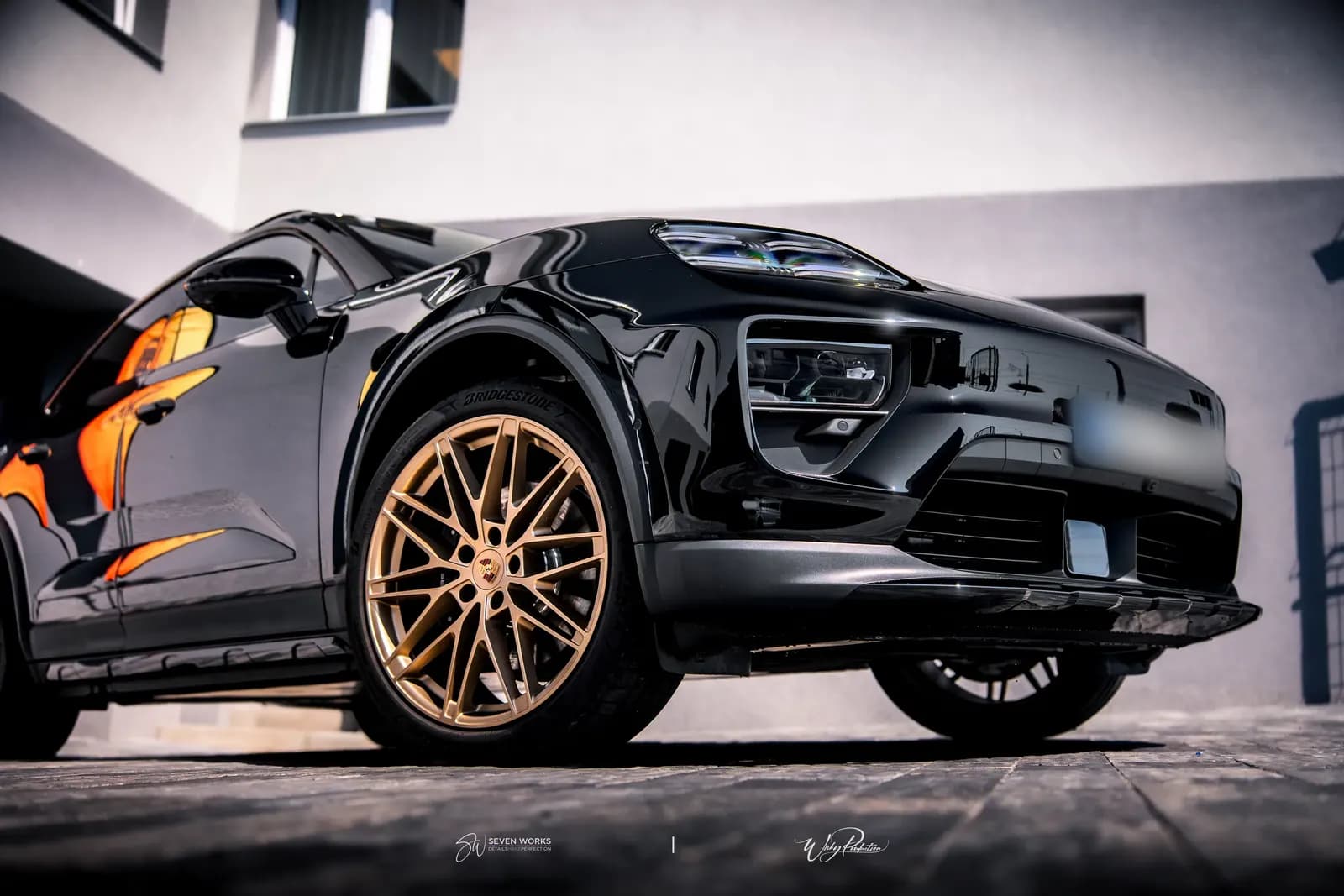 Close-up of the front wheel of a black Porsche with a gold rim and Bridgestone tyre.