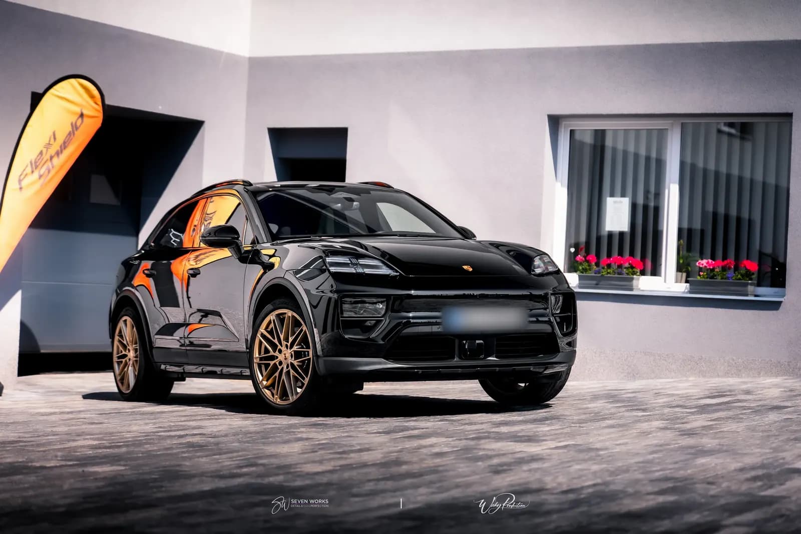 Black Porsche SUV from the front outside the workshop, Flexi Shield flag banner behind.