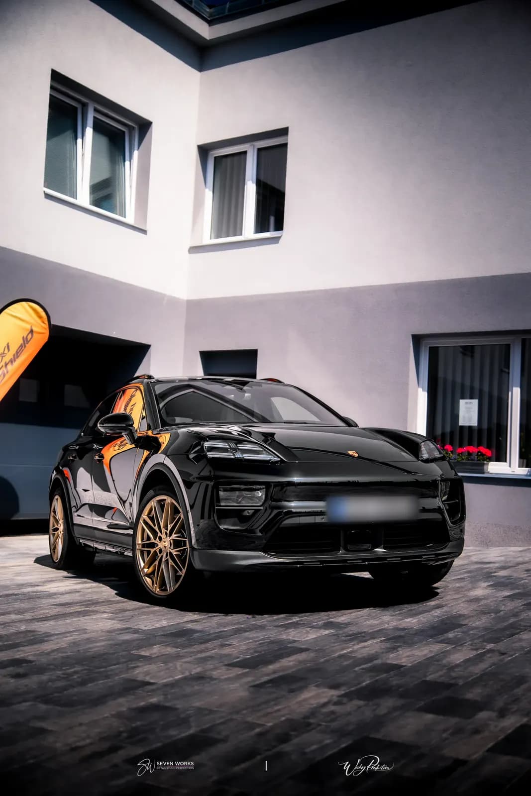 Black Porsche SUV from a front angle, portrait format, outside the building.