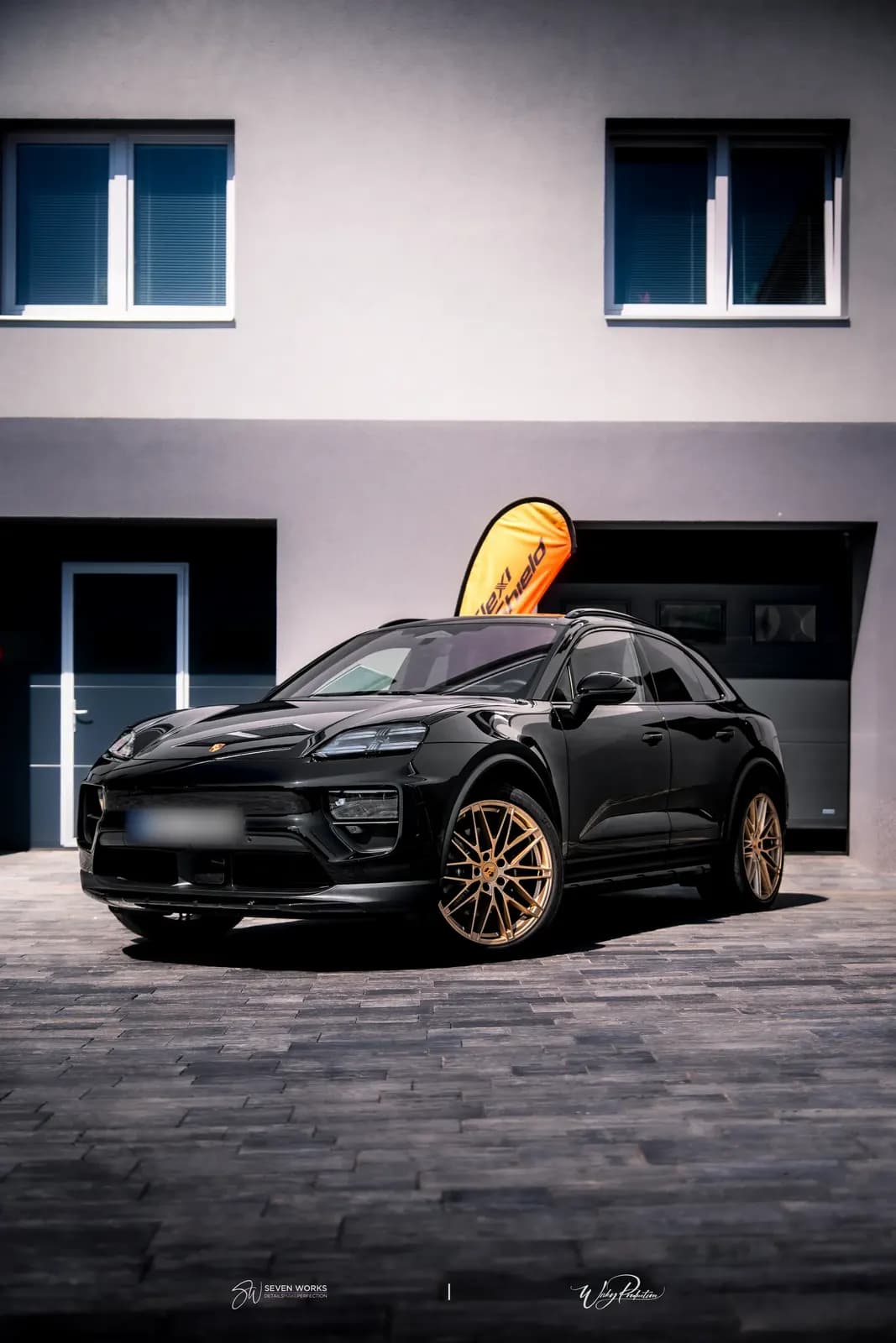 Front view of a black Porsche SUV in portrait format with garage doors behind.
