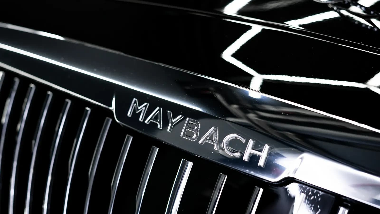 Close-up of a chrome radiator grille with a Maybach badge on a black car.