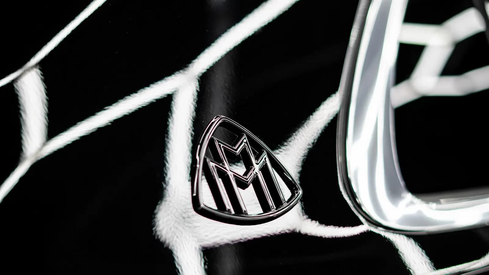 Close-up of a Maybach emblem on glossy black paint next to chrome trim.