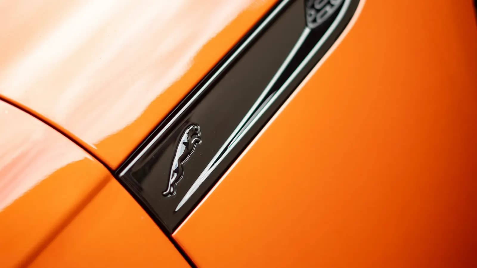 Close-up of the Jaguar emblem on the side vent of an orange car's front wing.