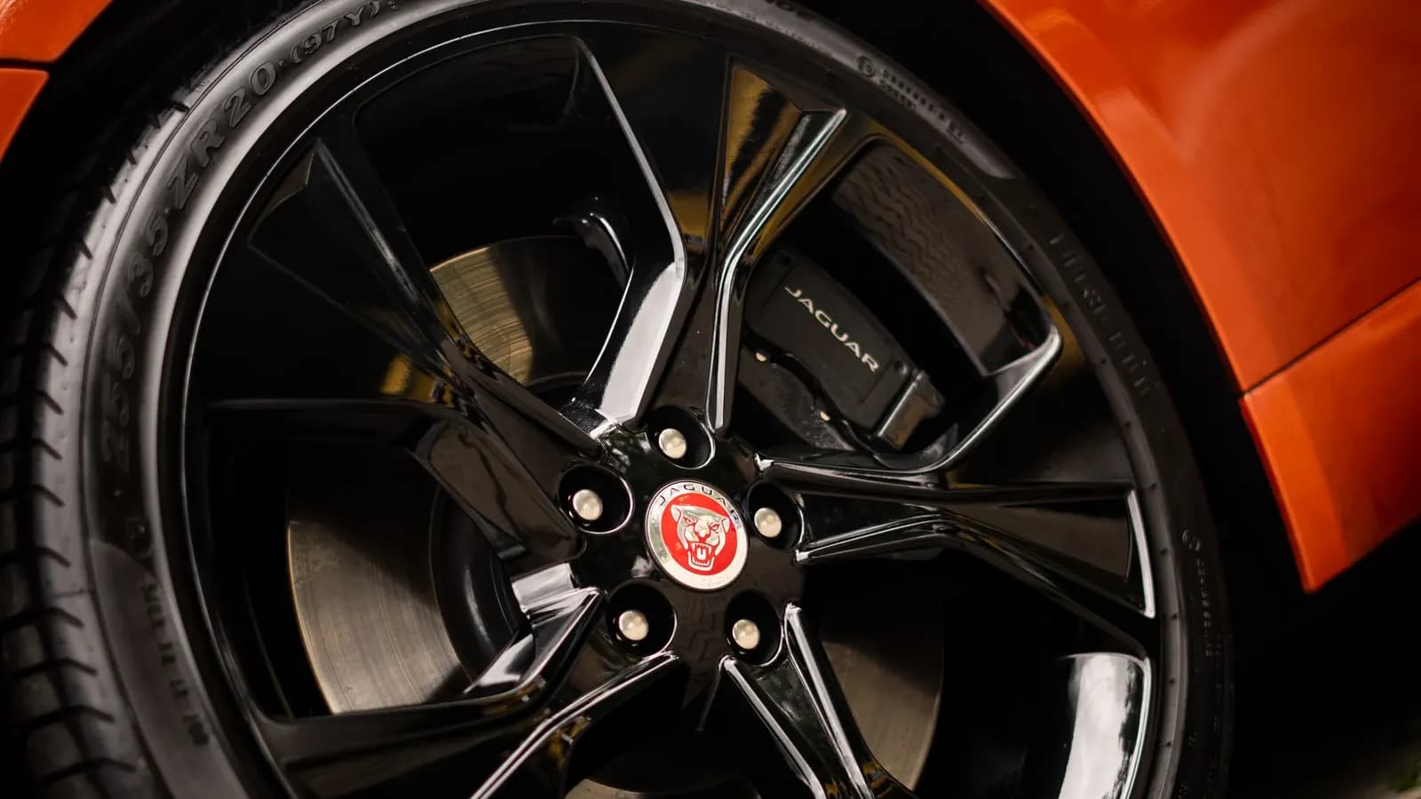 Close-up of the front wheel with a brake caliper and Jaguar lettering on an orange car.