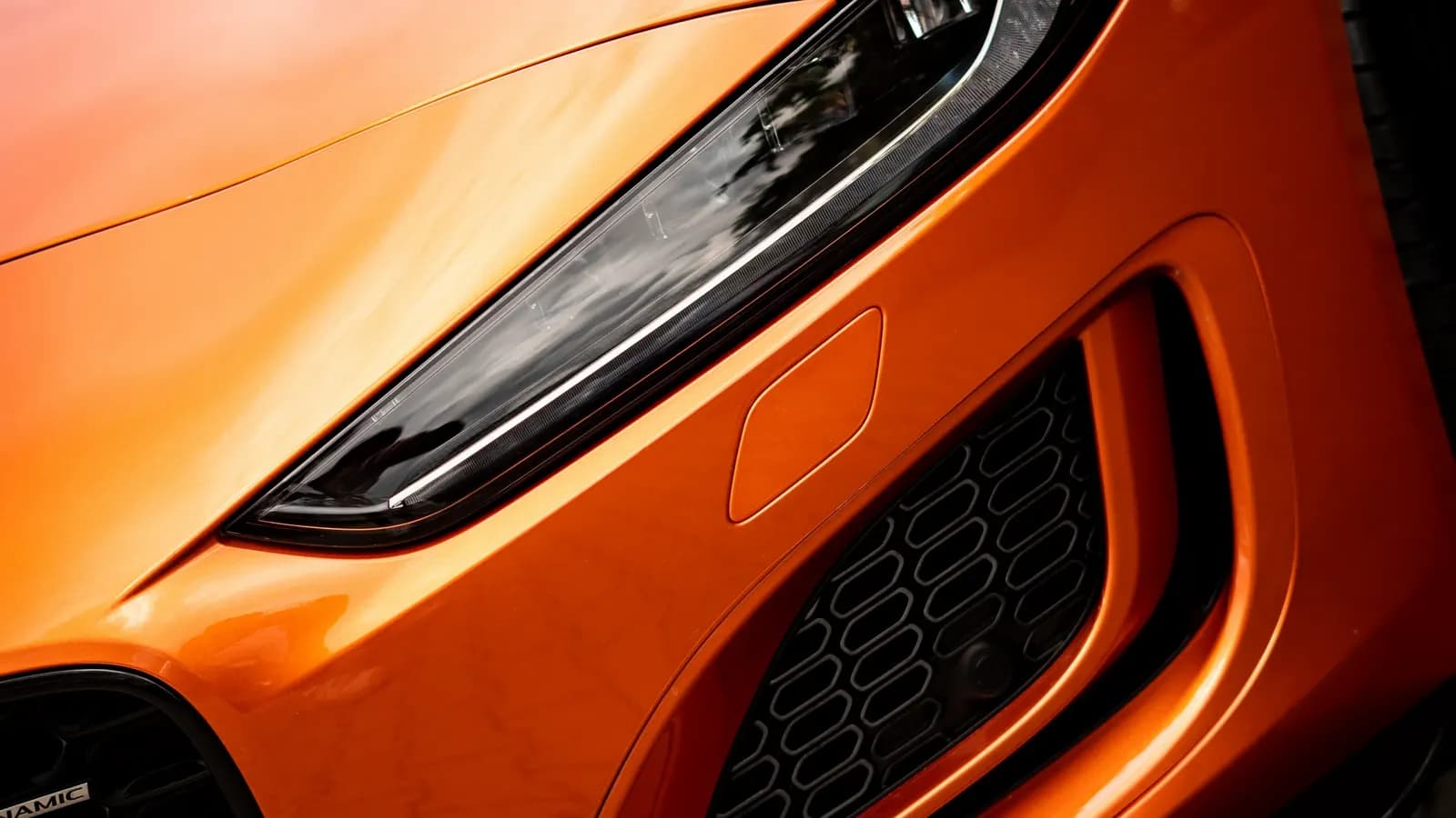 Close-up of the front headlight and grille of an orange car.