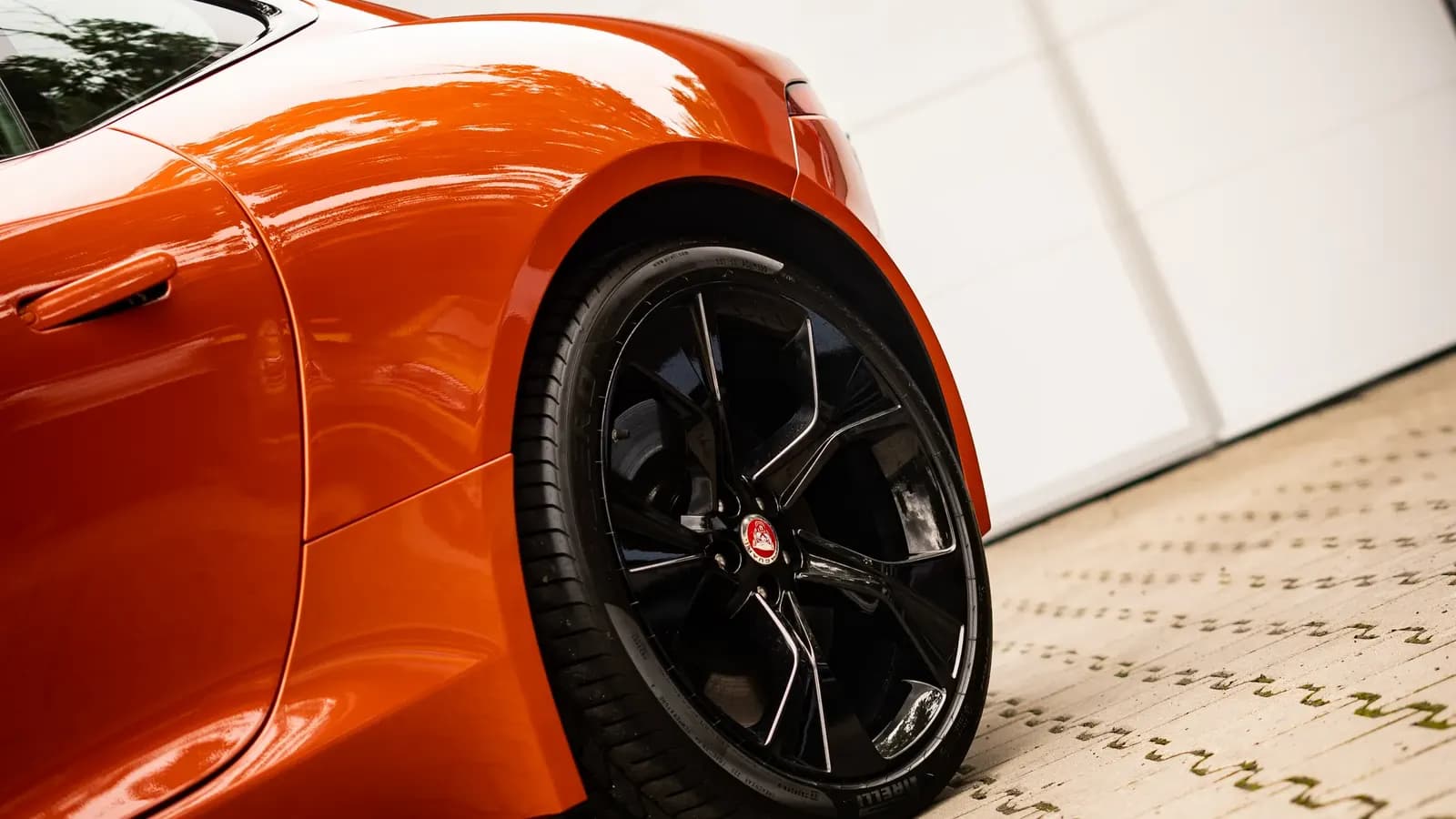 Close-up of the rear wing and wheel of an orange sports car with glossy paint.