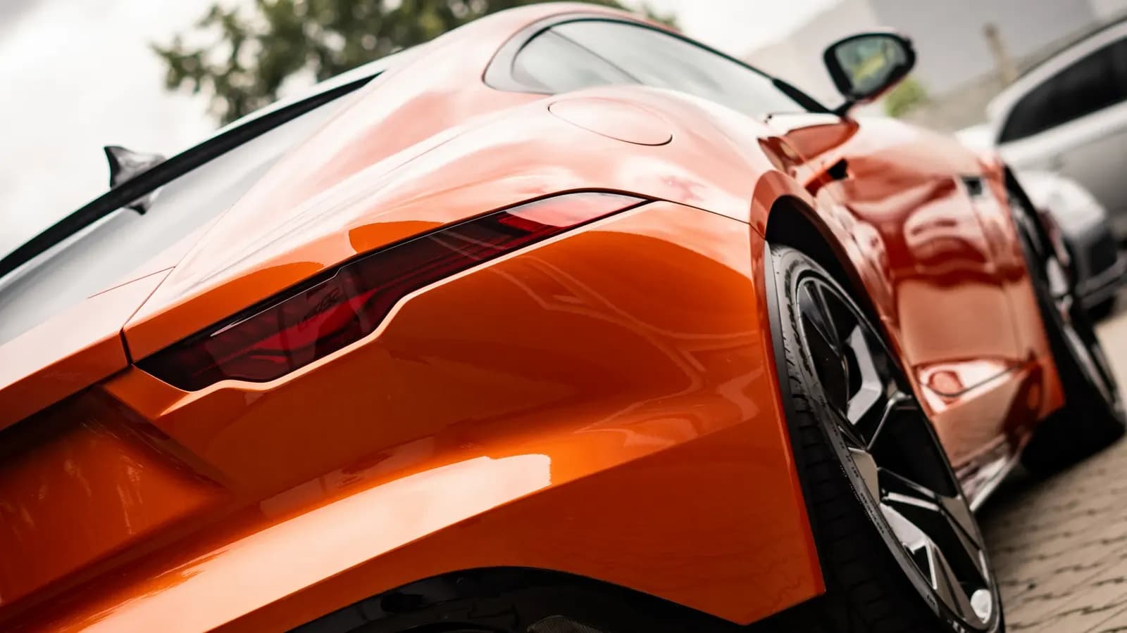 Close-up of the rear quarter panel and tail light of an orange sports car with high-gloss paint.
