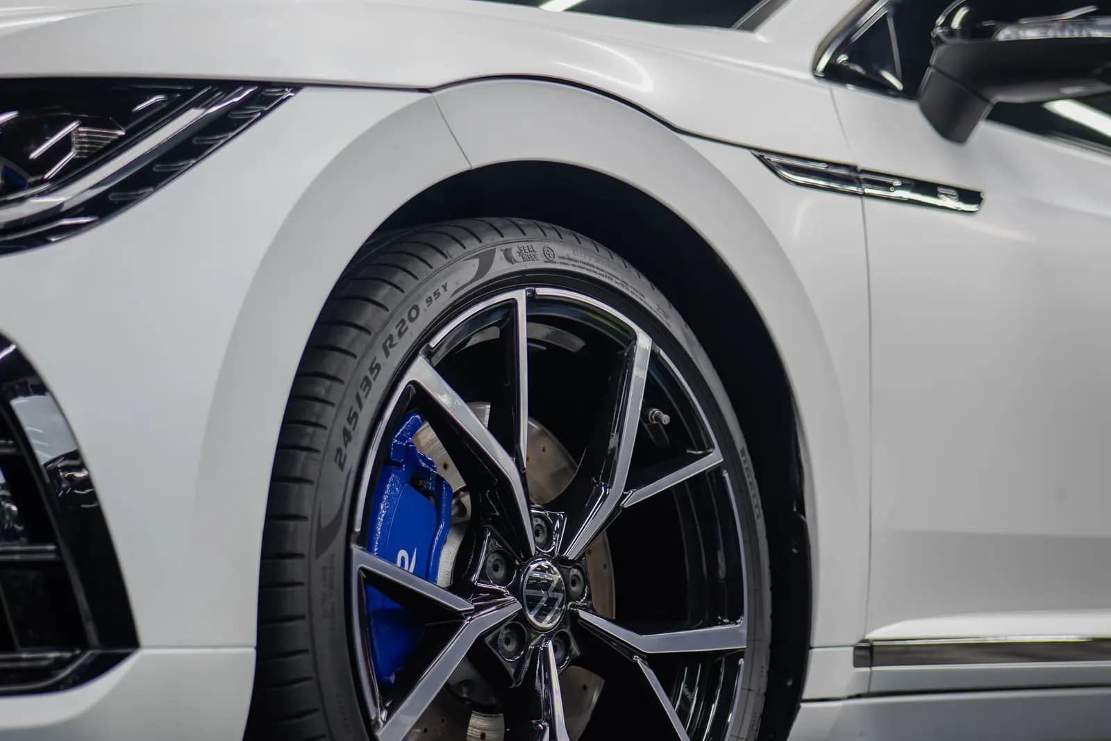 Detail předního kola bílého vozu s modrým brzdovým třmenem v showroomu.