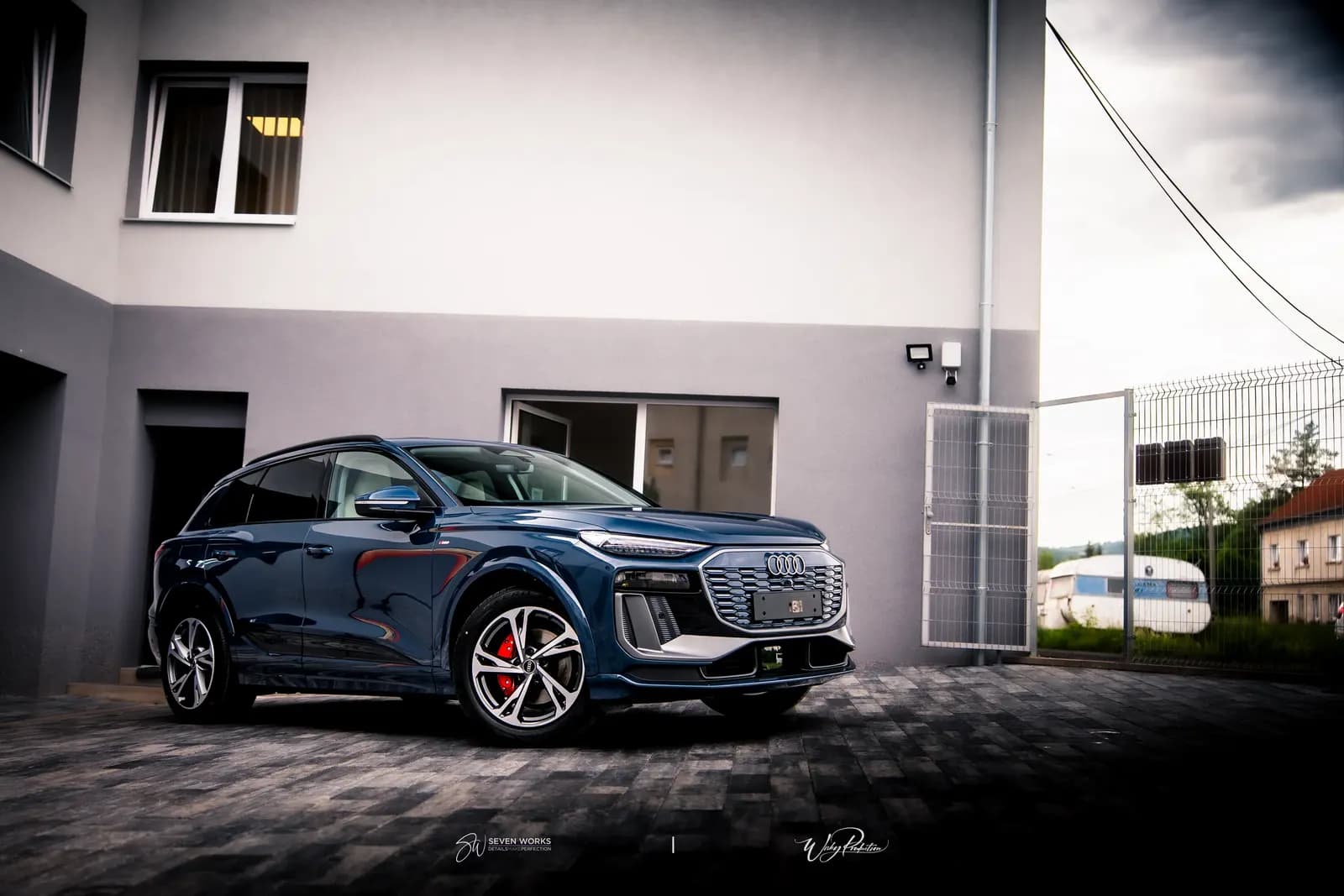 Tmavě modré Audi SUV zaparkované před domem v podvečerním světle, pohled zepředu z boku.
