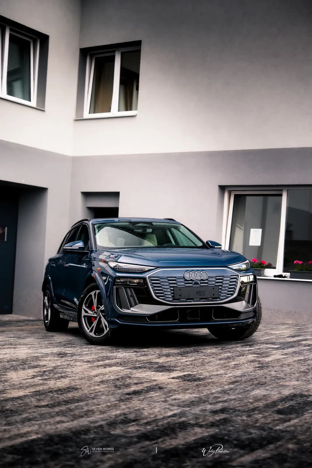 Tmavě modré Audi SUV zepředu zboku na nádvoří před domem.
