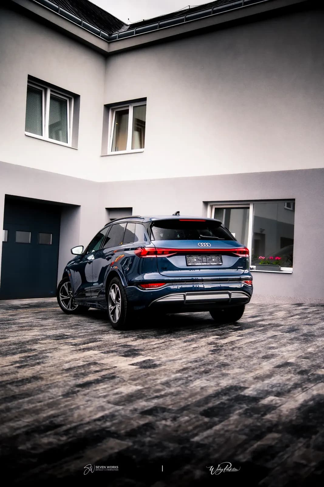 Zadní pohled na tmavě modré Audi SUV s logem Audi, zaparkované před domem.