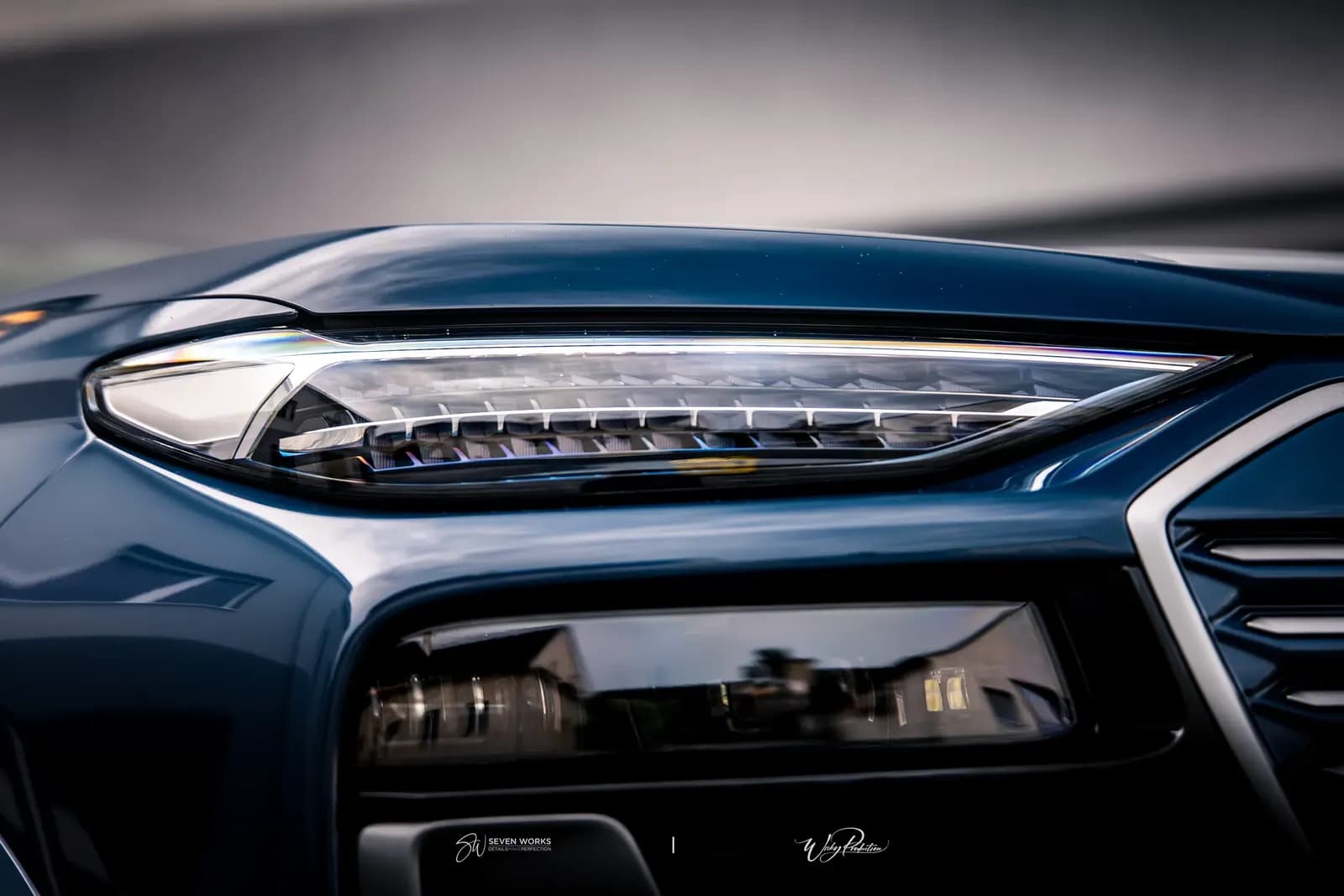 Makro detail rozsvíceného předního světla tmavě modrého Audi SUV.