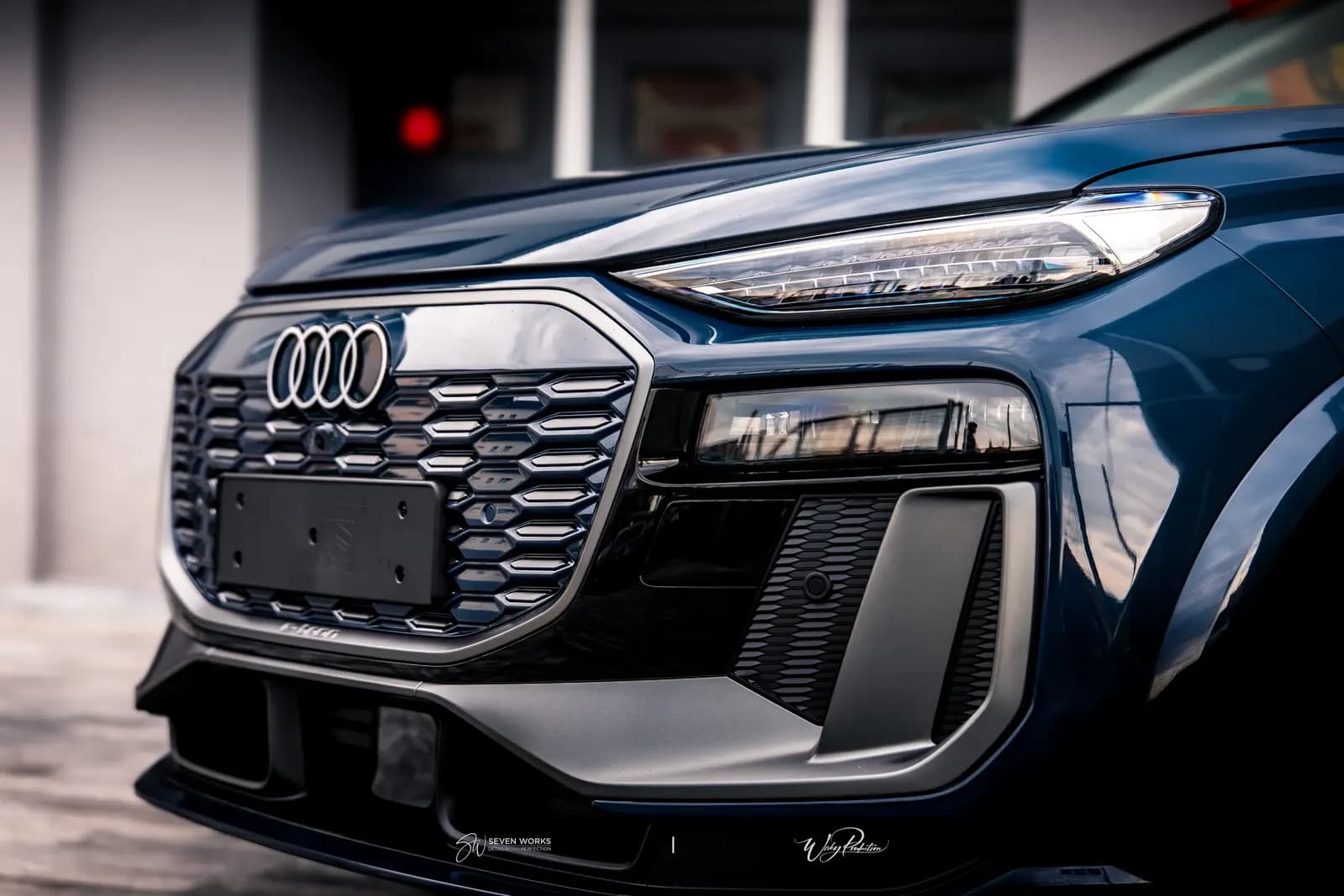 Detail přední masky s logem Audi a světlometem tmavě modrého SUV.