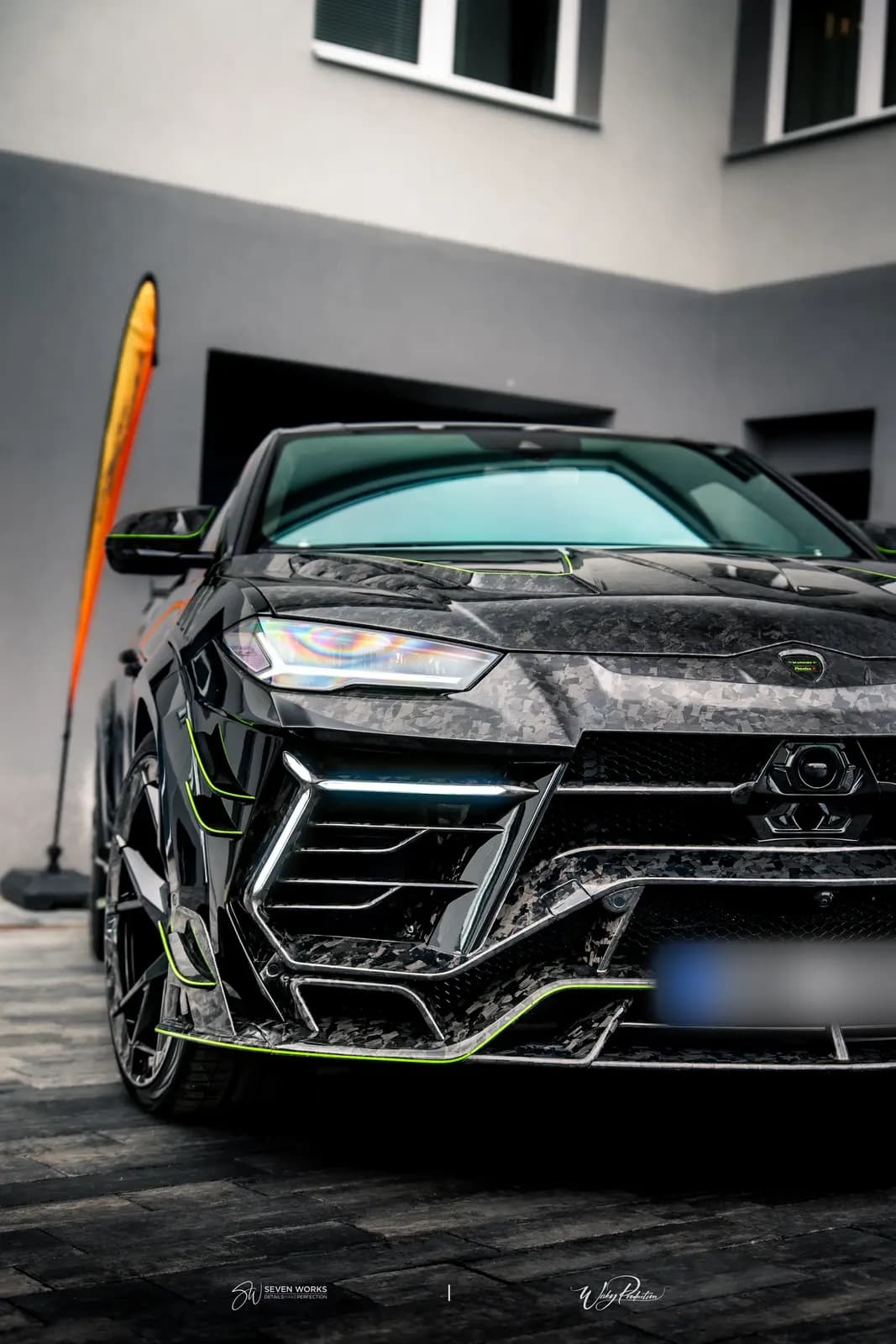 Čelní pohled na karbonovou přední masku Lamborghini Urus s LED světlomety před budovou.