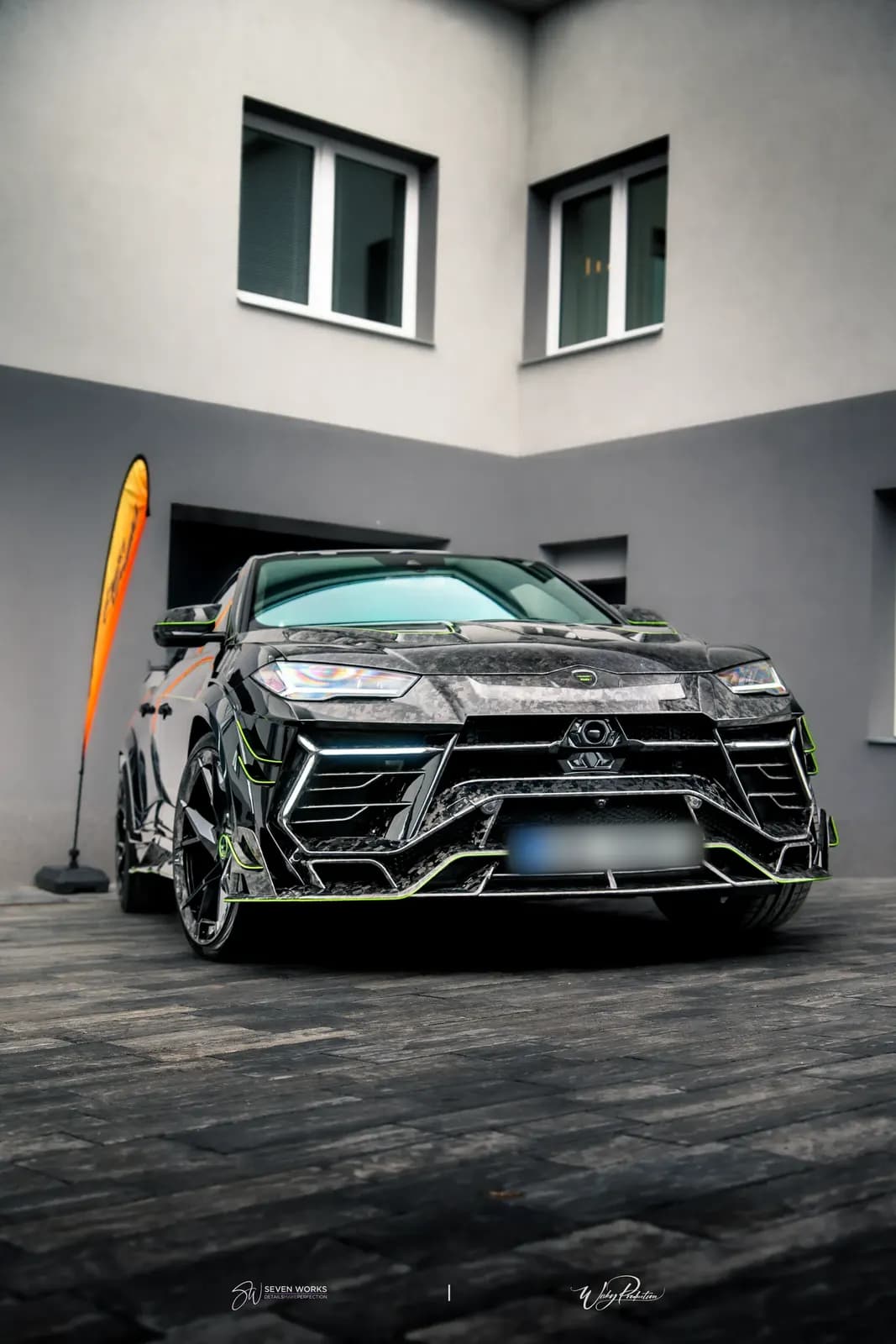 Lamborghini Urus s karbonovým widebody kitem, čelní pohled na nádvoří s reklamním vlajkovým bannerem.