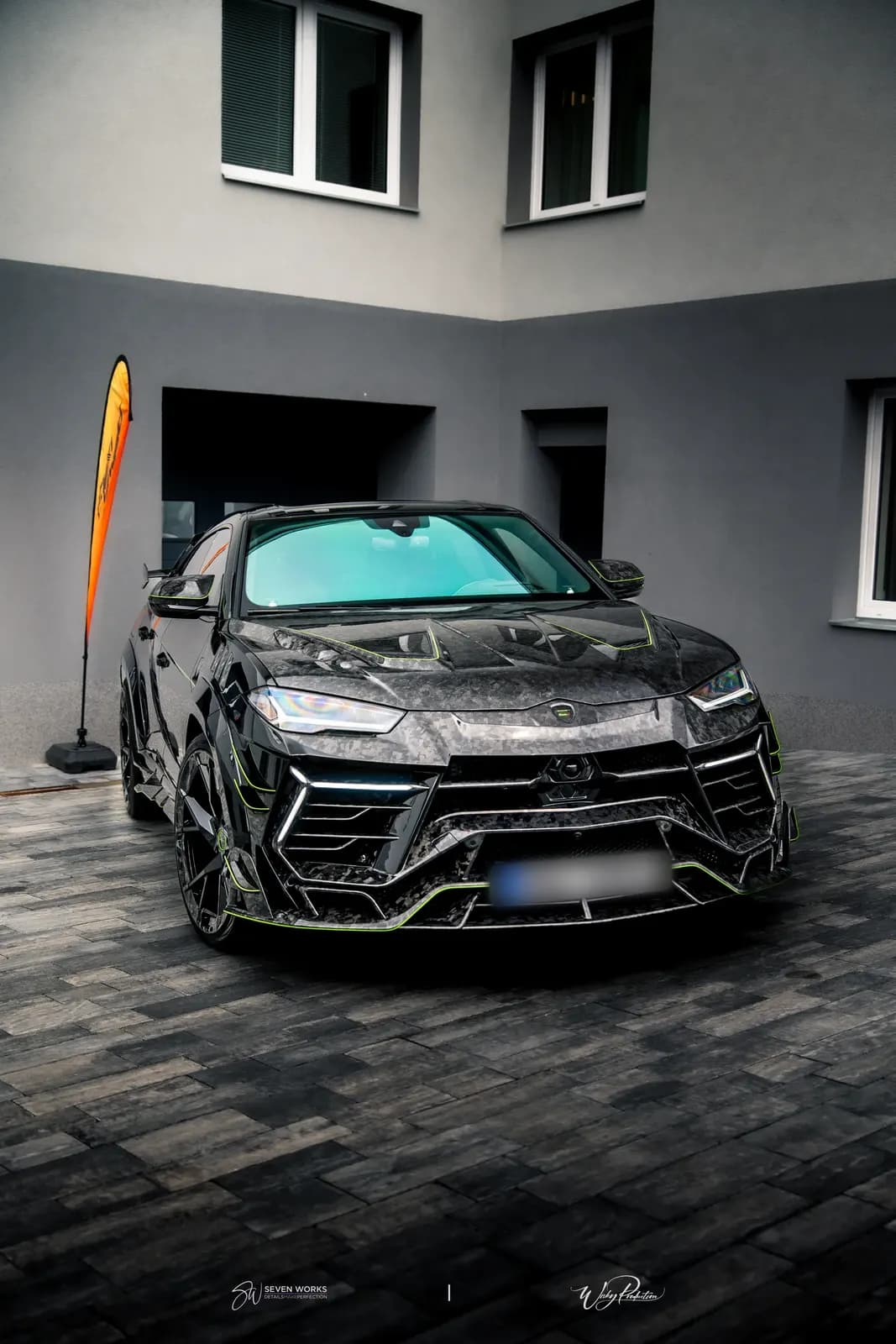 Lamborghini Urus zepředu na dlážděném nádvoří před vícepodlažní budovou.